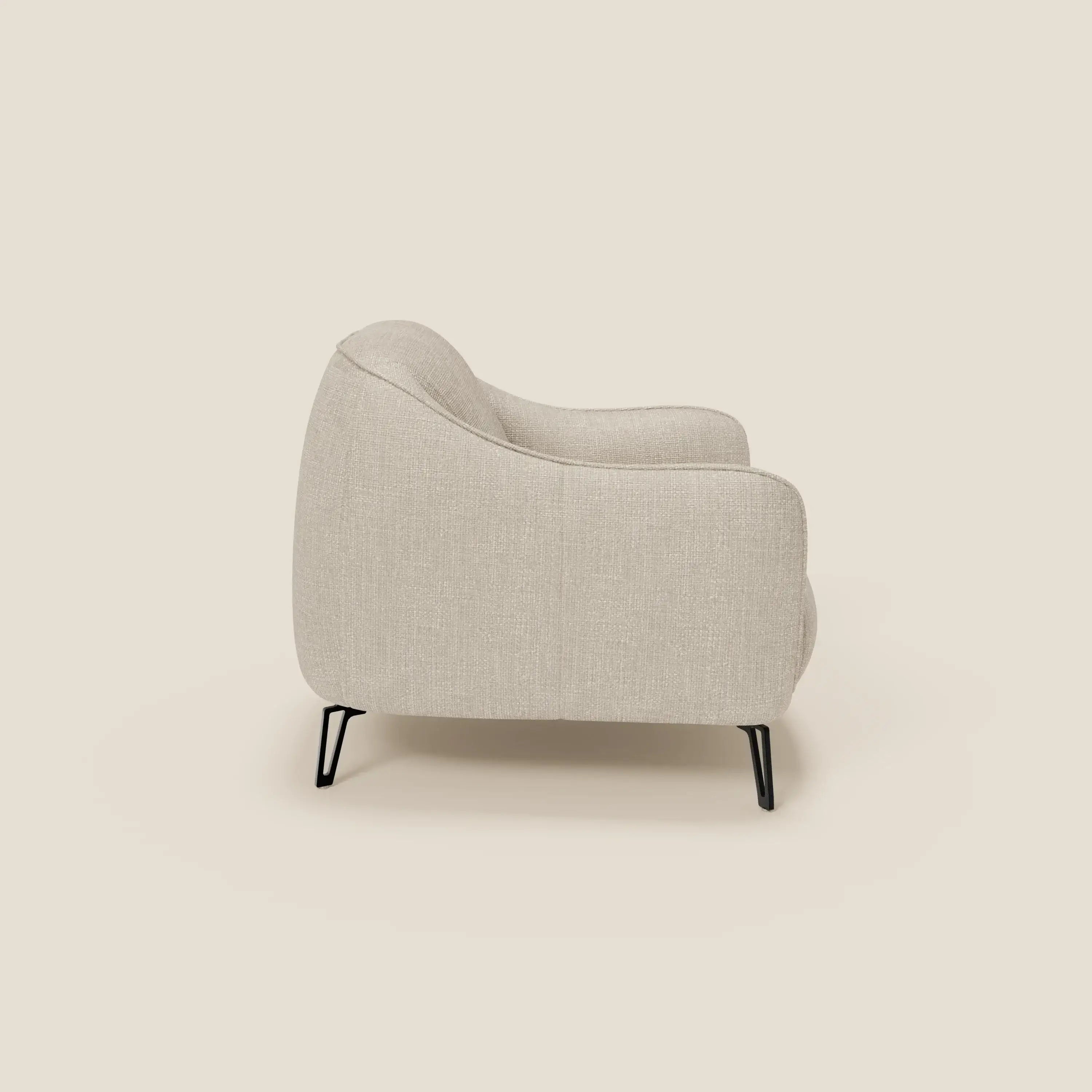 La poltroncina Avela di Divani.Store, vista di lato su uno sfondo a tinta unita, è caratterizzata da tessuto morbido impermeabile T06 panna, curve morbide, imbottitura soffice e sottili gambe in metallo nero per un comfort senza tempo e uno stile minimalista.