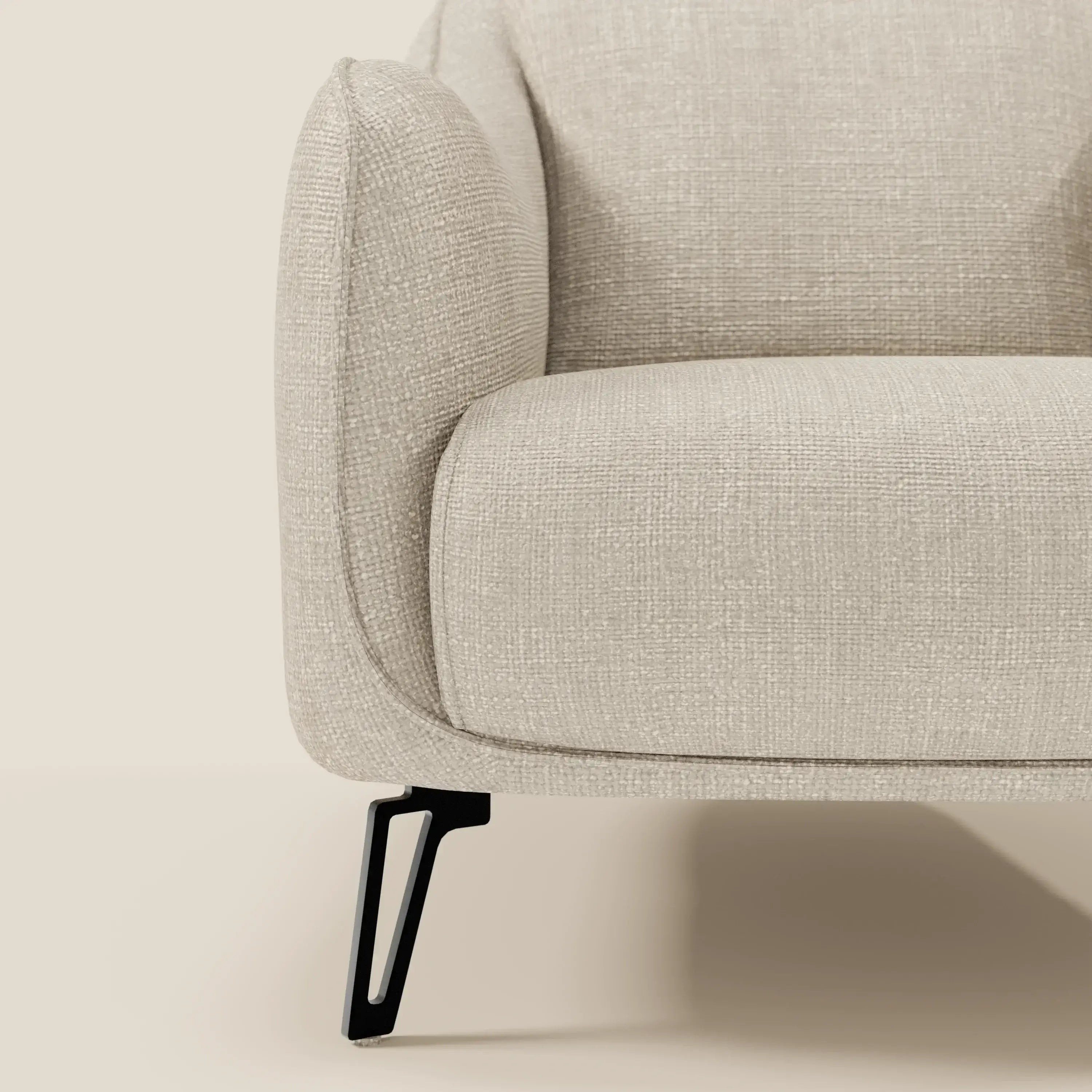 Primo piano della poltroncina Avela di Divani.Store in morbido tessuto impermeabile T06 panna, che mette in evidenza il bracciolo sinistro e il cuscino della seduta con le eleganti gambe angolate in metallo nero: un design moderno dal comfort senza tempo.