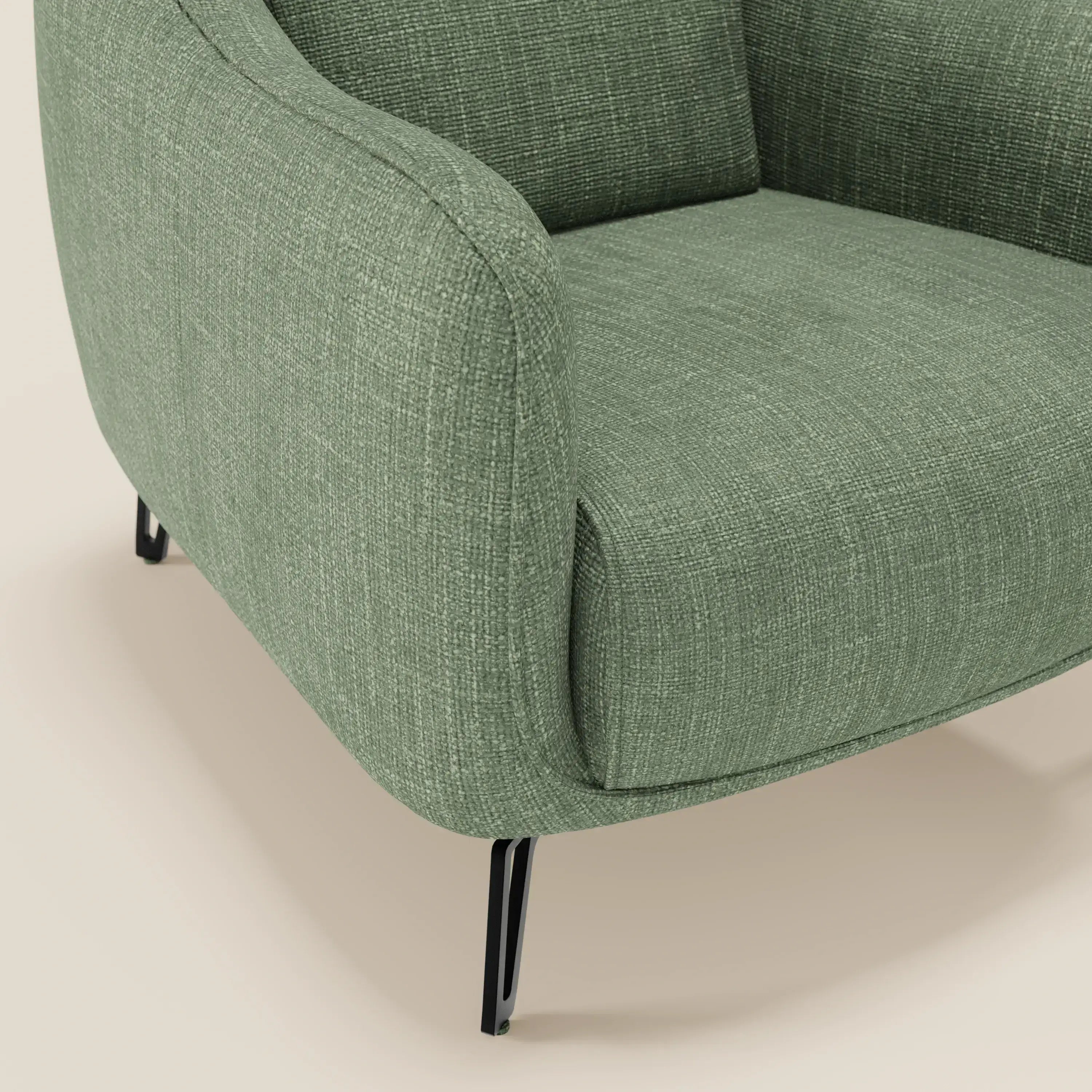Primo piano di Avela Poltroncina di Divani.Store, in morbido tessuto impermeabile T06 verde, con braccioli delicatamente curvati e sottili gambe angolate in metallo nero, su uno sfondo beige neutro.