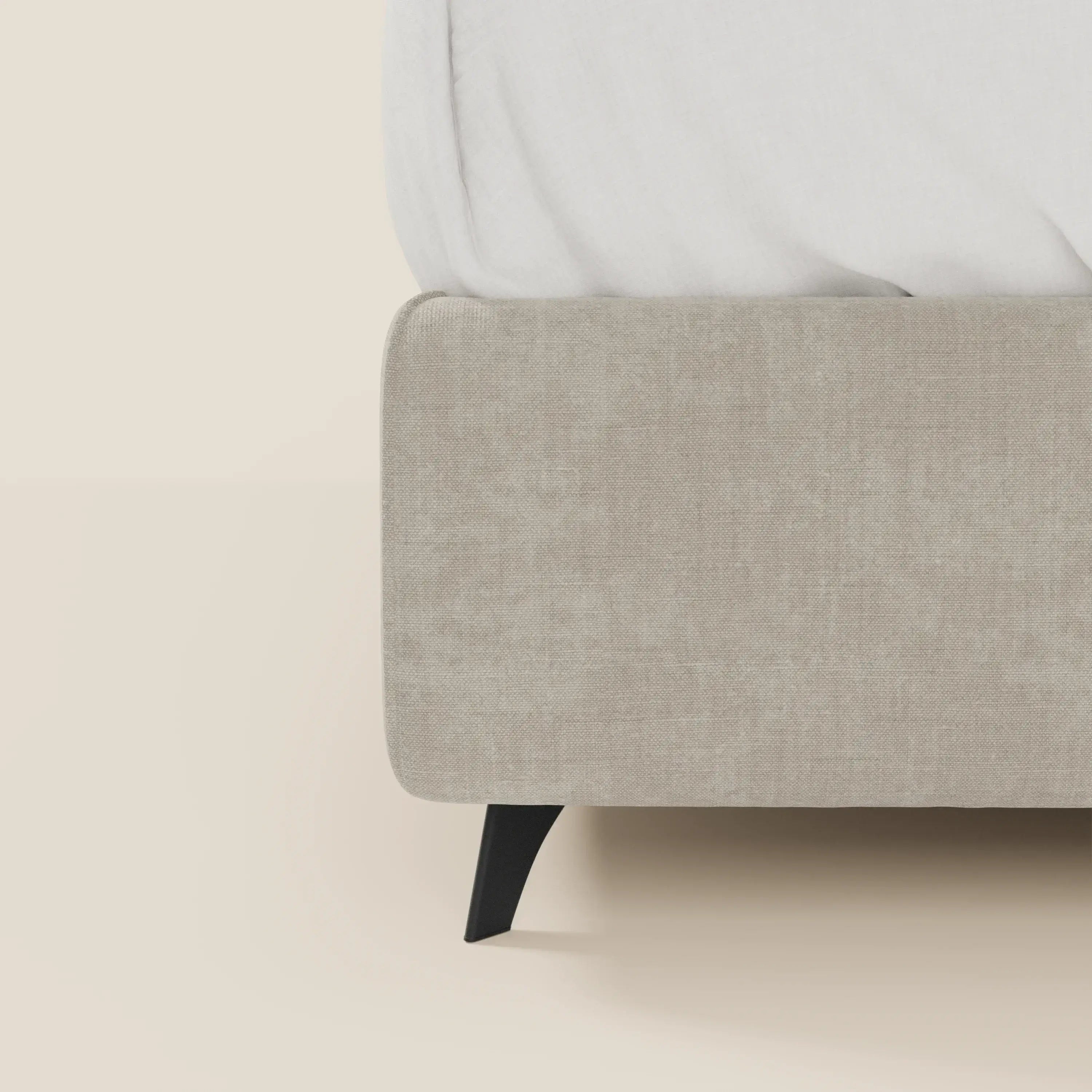 Primo piano del letto contenitore Bogart Edizione Grande Fratello di Letti.store, con struttura in tessuto antimacchia T22 panna beige e gamba angolare nera. Presentato con biancheria da letto bianca, offre un look elegante e moderno su pareti e pavimenti chiari.