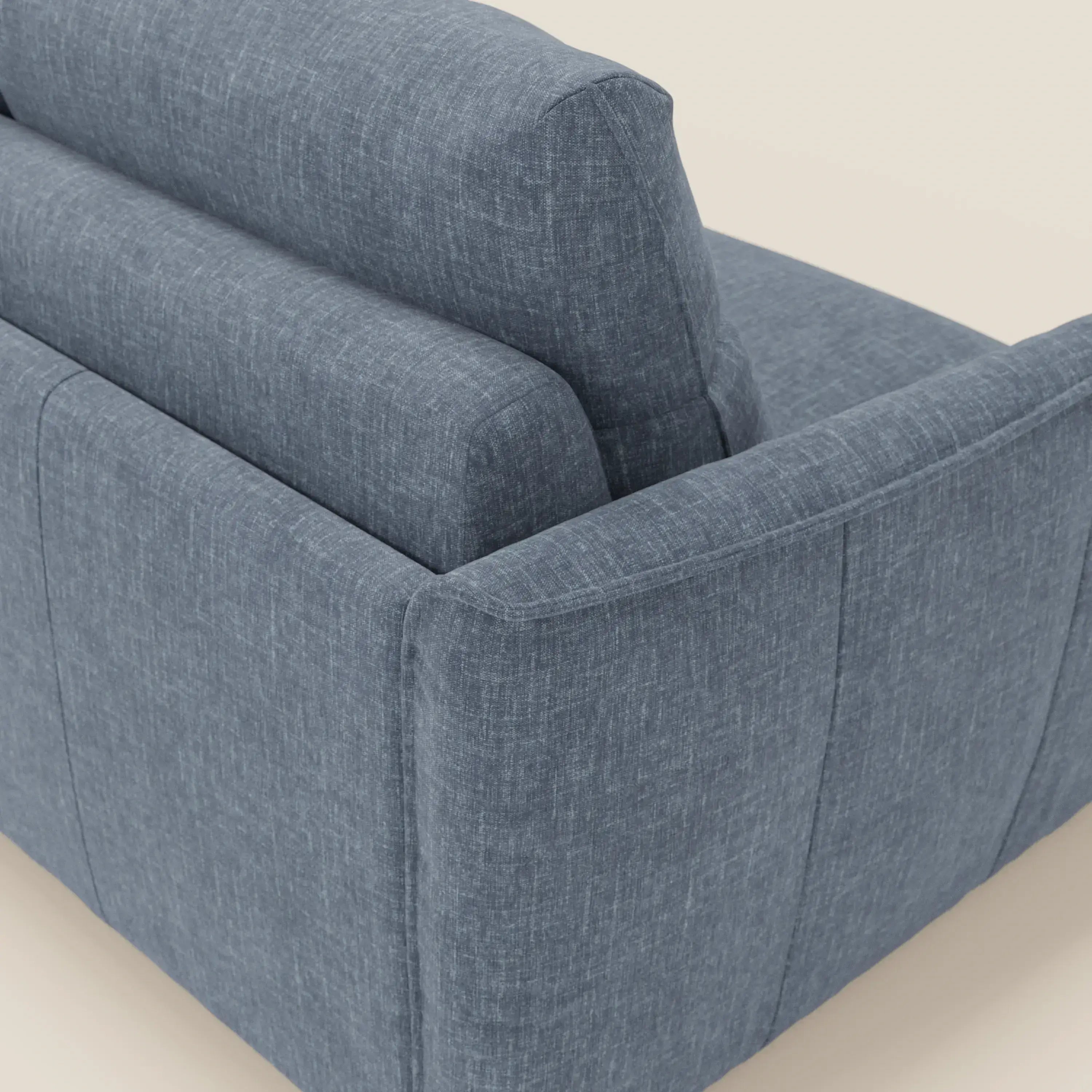 Primo piano dello schienale e del bracciolo del divano letto Elios con morbidi cuscini spalliera in tessuto smacchiabile T24 blu ardesia di Divani.Store, che mostra le sue linee pulite e i suoi cuscini in feltro su uno sfondo neutro.