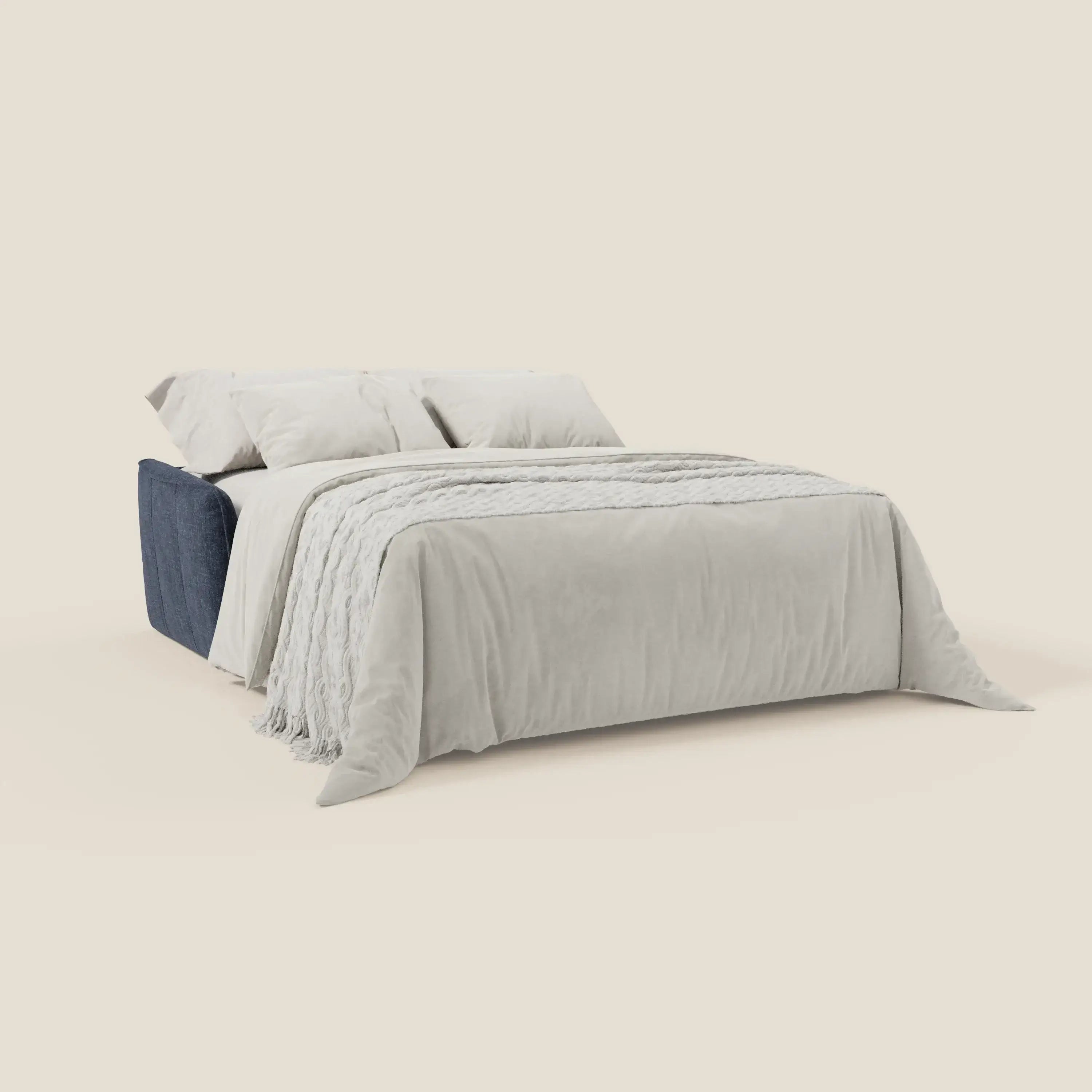 Divano letto Elios di Divani.Store con base in tessuto smacchiabile T24 blu notte, morbidi cuscini spalliera, biancheria grigia e due cuscini. Un plaid testurizzato con frange arricchisce il design essenziale su sfondo beige.