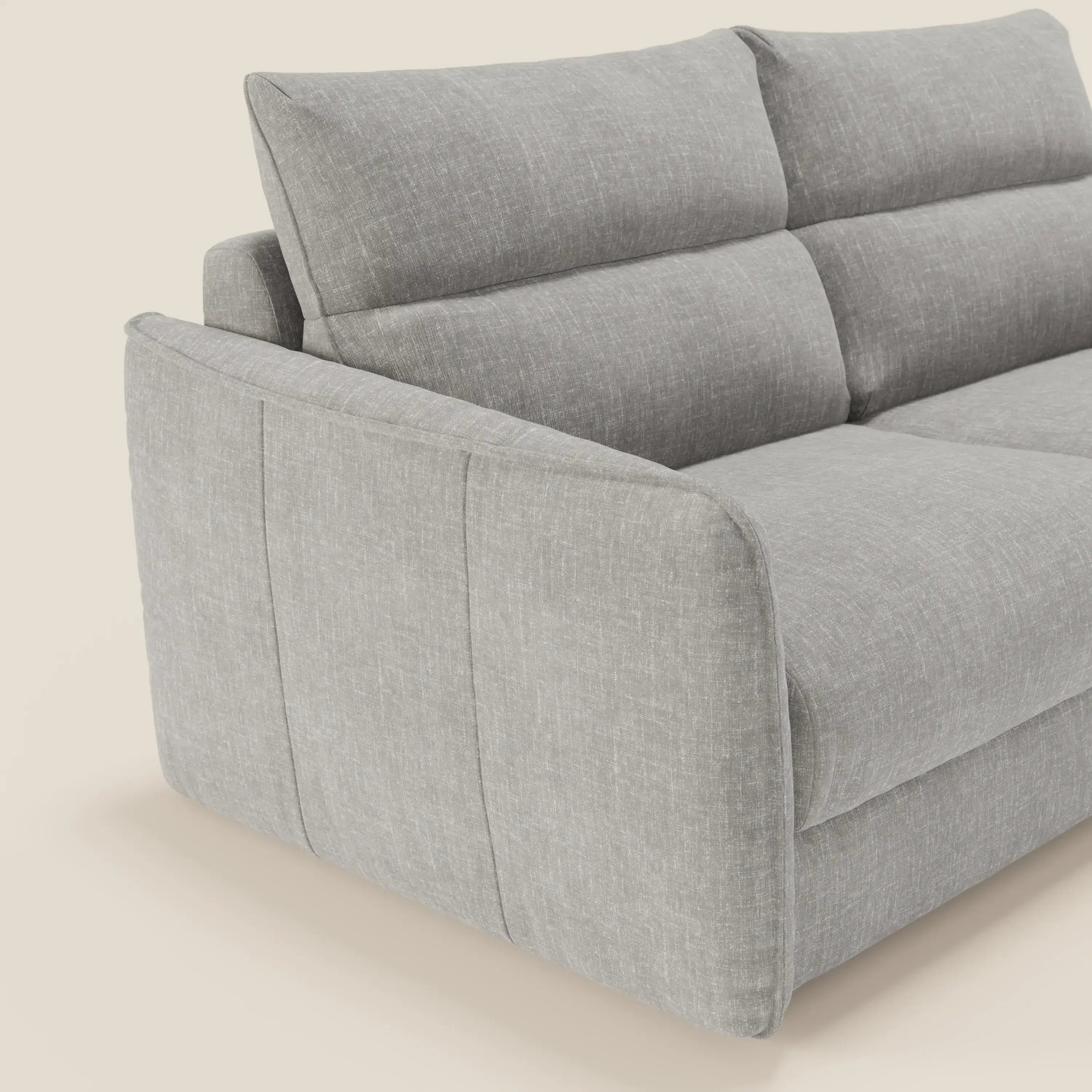 Il divano letto Elios di Divani.Store, presentato in tessuto smacchiabile grigio chiaro T24 con morbidi cuscini di schienale segmentati e ampi braccioli, si staglia su uno sfondo bianco sporco. È visibile solo una parte del divano moderno.