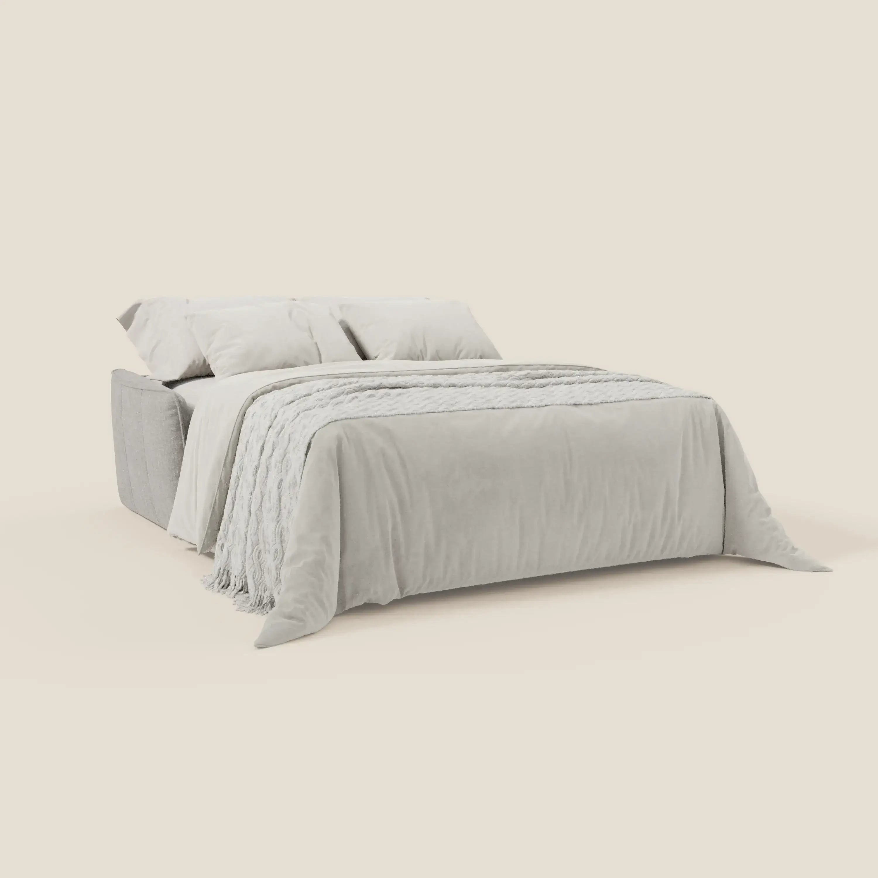 Il Divano Elios letto con morbidi cuscini spalliera in tessuto smacchiabile T24 grigio di Divani.Store, moderno e basso, con due grandi cuscini, plaid testurizzato e copriletto soffice su sfondo crema.