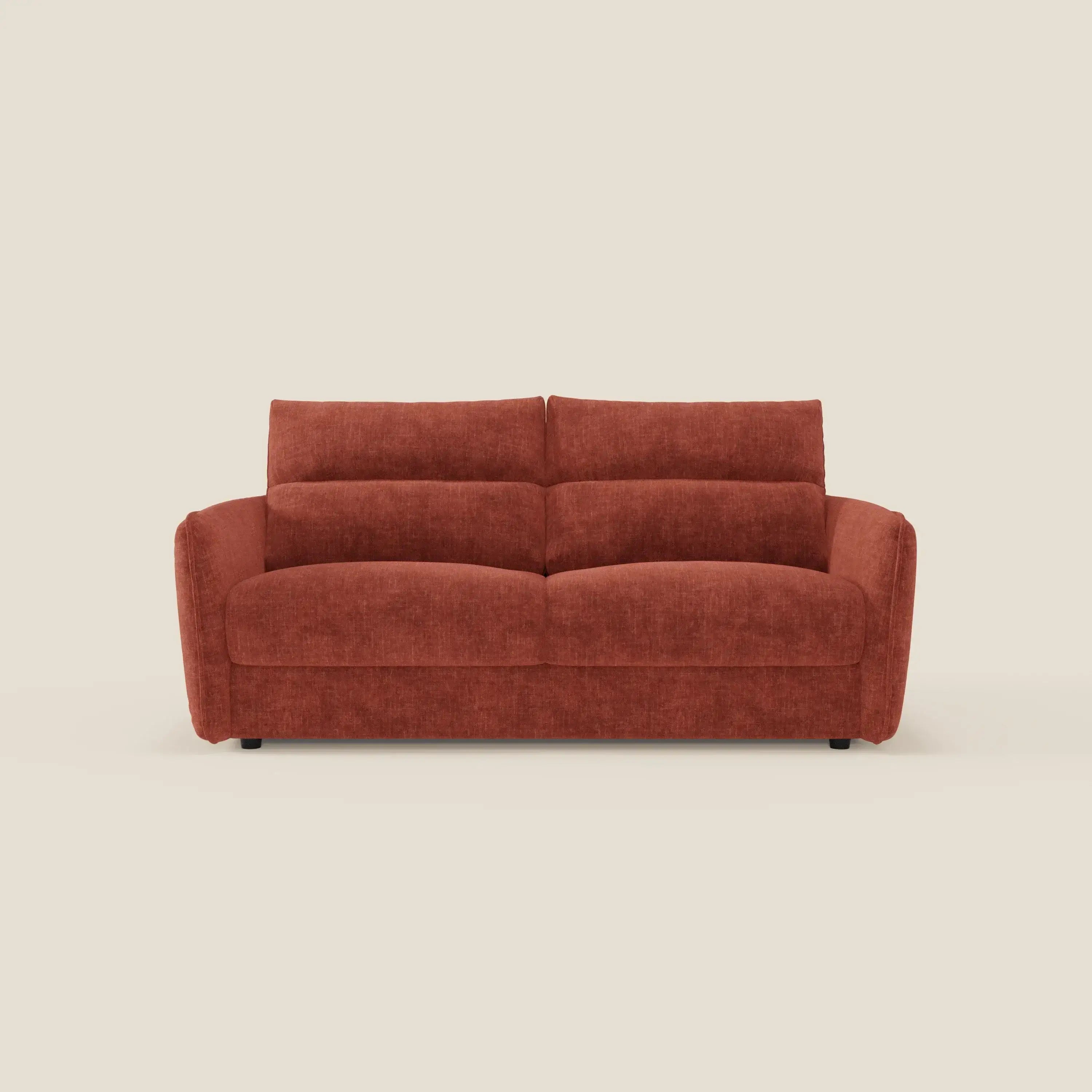 Il divano letto Elios di Divani.Store, in tessuto smacchiabile T24 ruggine, è caratterizzato da spalliere di cuscini morbidi, braccioli arrotondati e un design contemporaneo e minimalista, presentato frontalmente su uno sfondo crema.