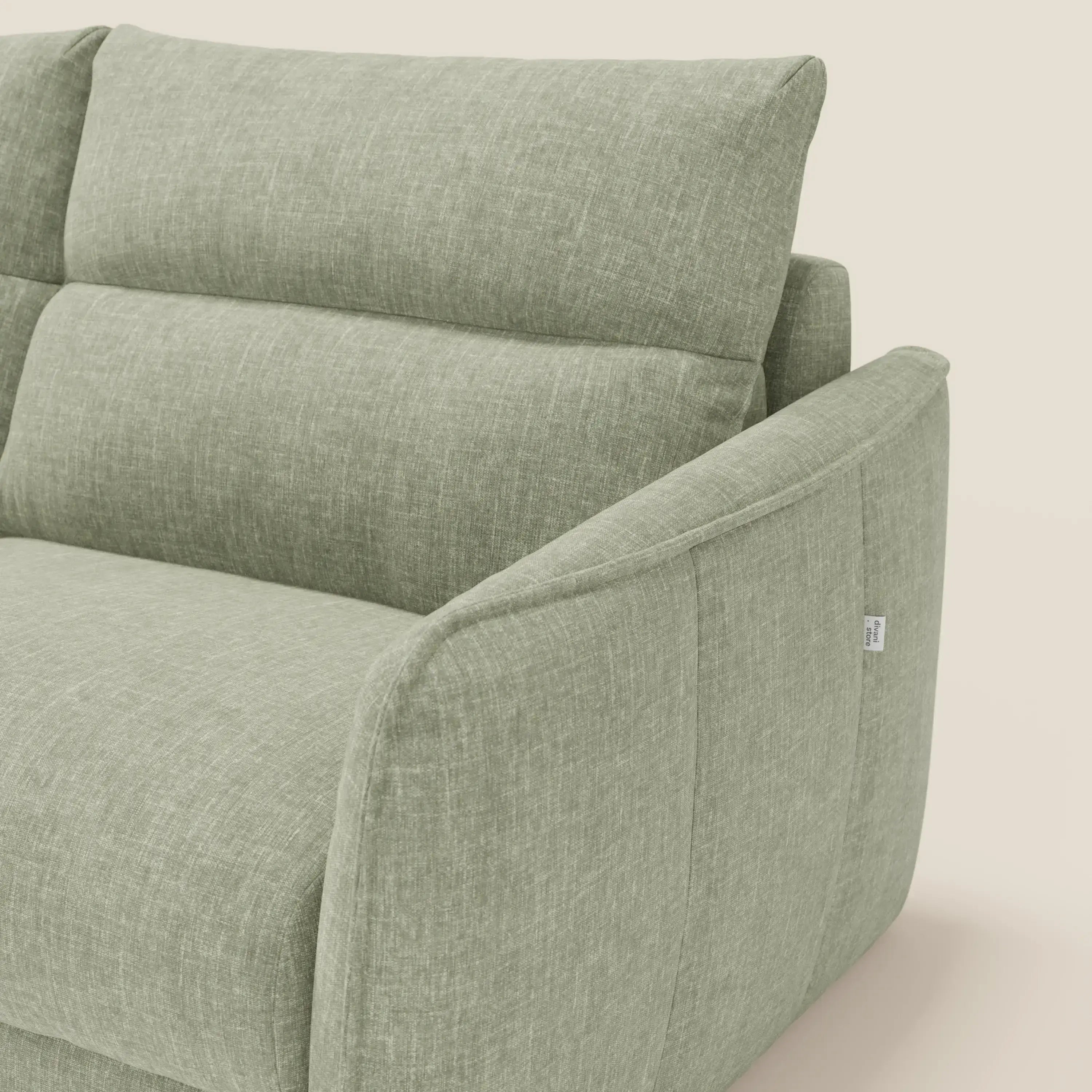 Primo piano del Divano letto Elios di Divani.Store in tessuto smacchiabile T24 verde salvia, caratterizzato da cuscini dello schienale, braccioli angolati, cuciture a vista e una piccola etichetta bianca sulla cucitura esterna.