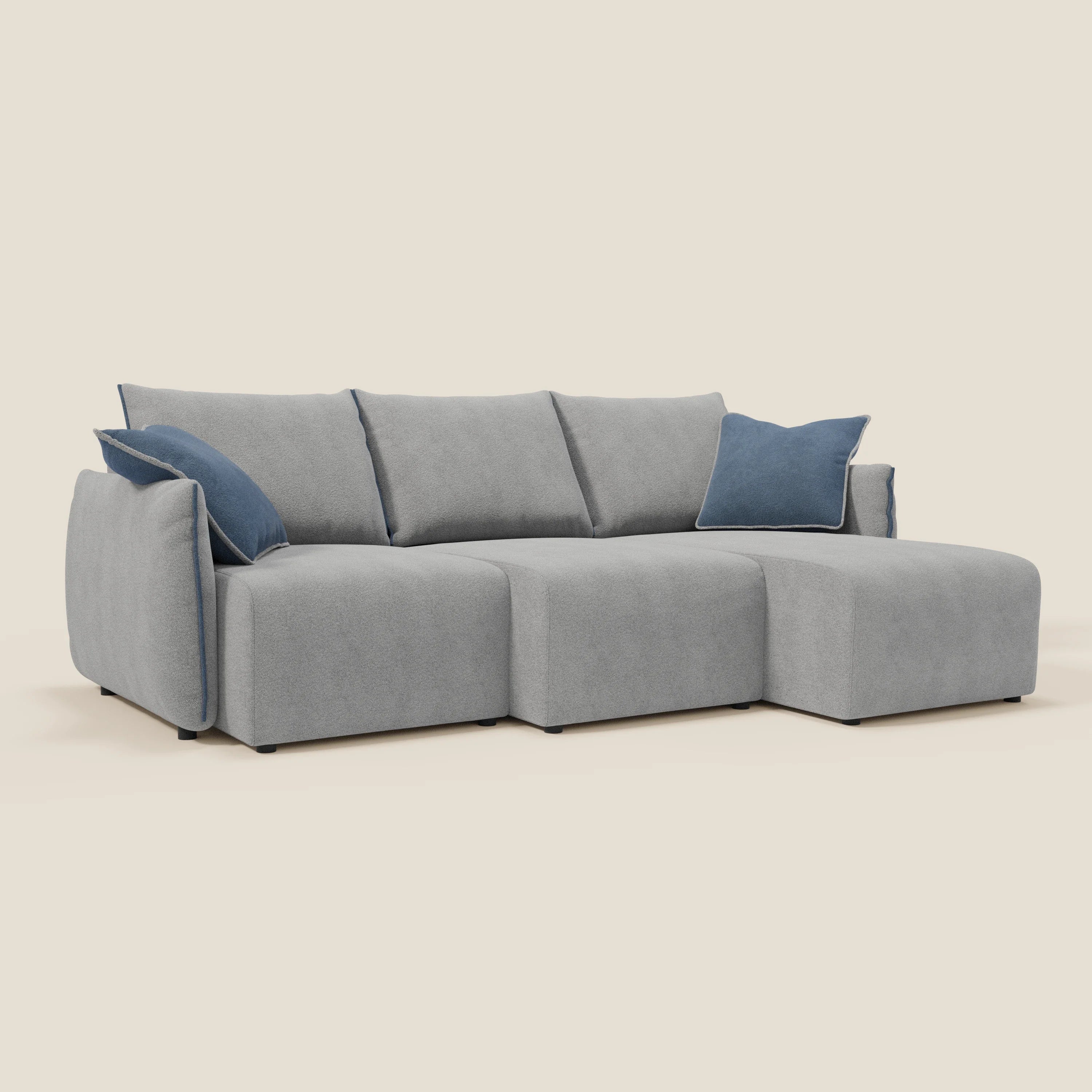 Il Divano angolare reversibile Flexar di Divani.Store è caratterizzato da tre sedute, una chaise lounge destra e sedute allungabili in morbido bouclé impermeabile T07 grigio-blu. Due cuscini blu spiccano su uno sfondo beige chiaro.