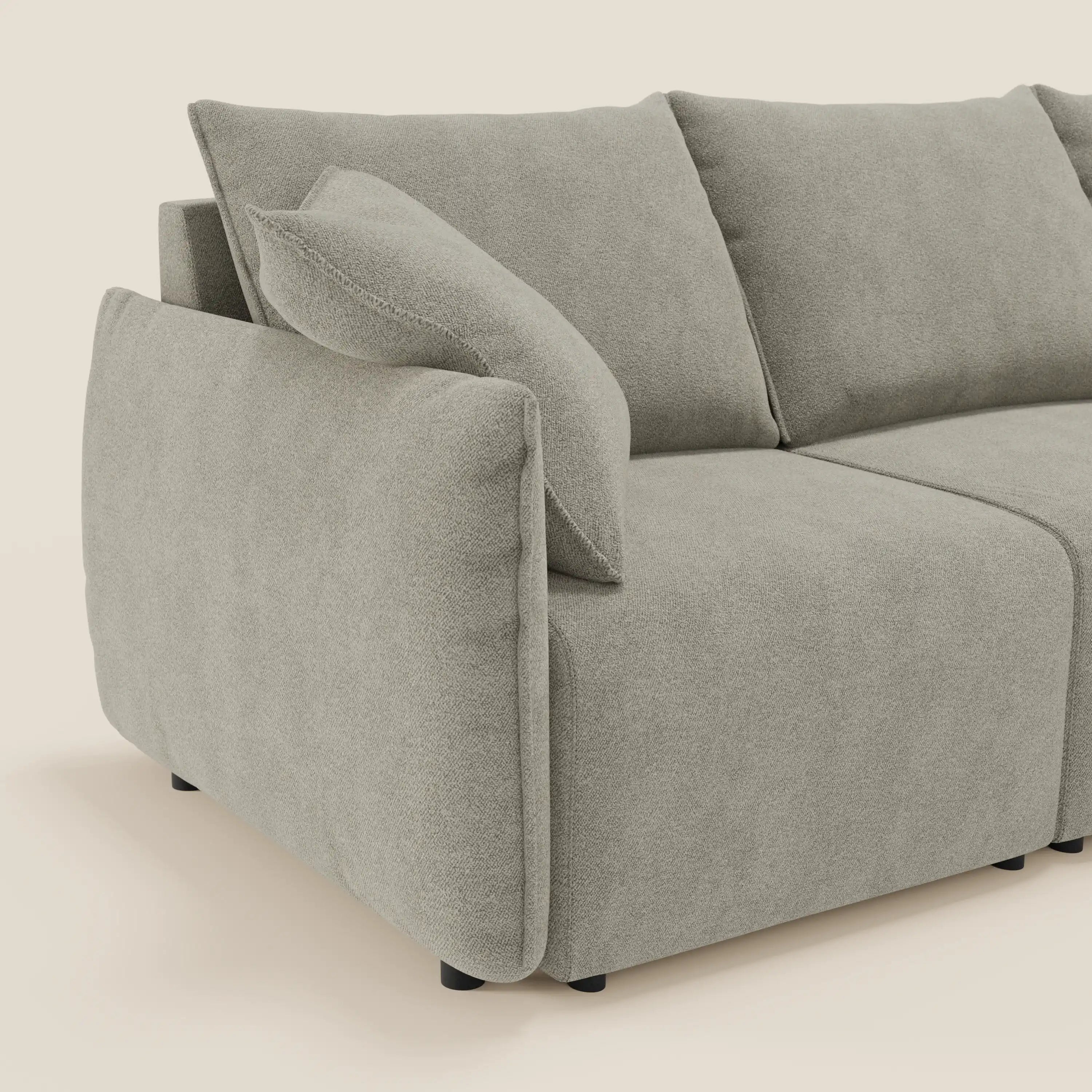 Primo piano del divano Flexar con 3 sedute allungabili di Divani.Store, in bouclé impermeabile T07 beige con schienale in piuma d'oca, cuscini in felpa, ampi braccioli imbottiti e gambe corte nere. Un cuscino libero poggia sul bracciolo sinistro.