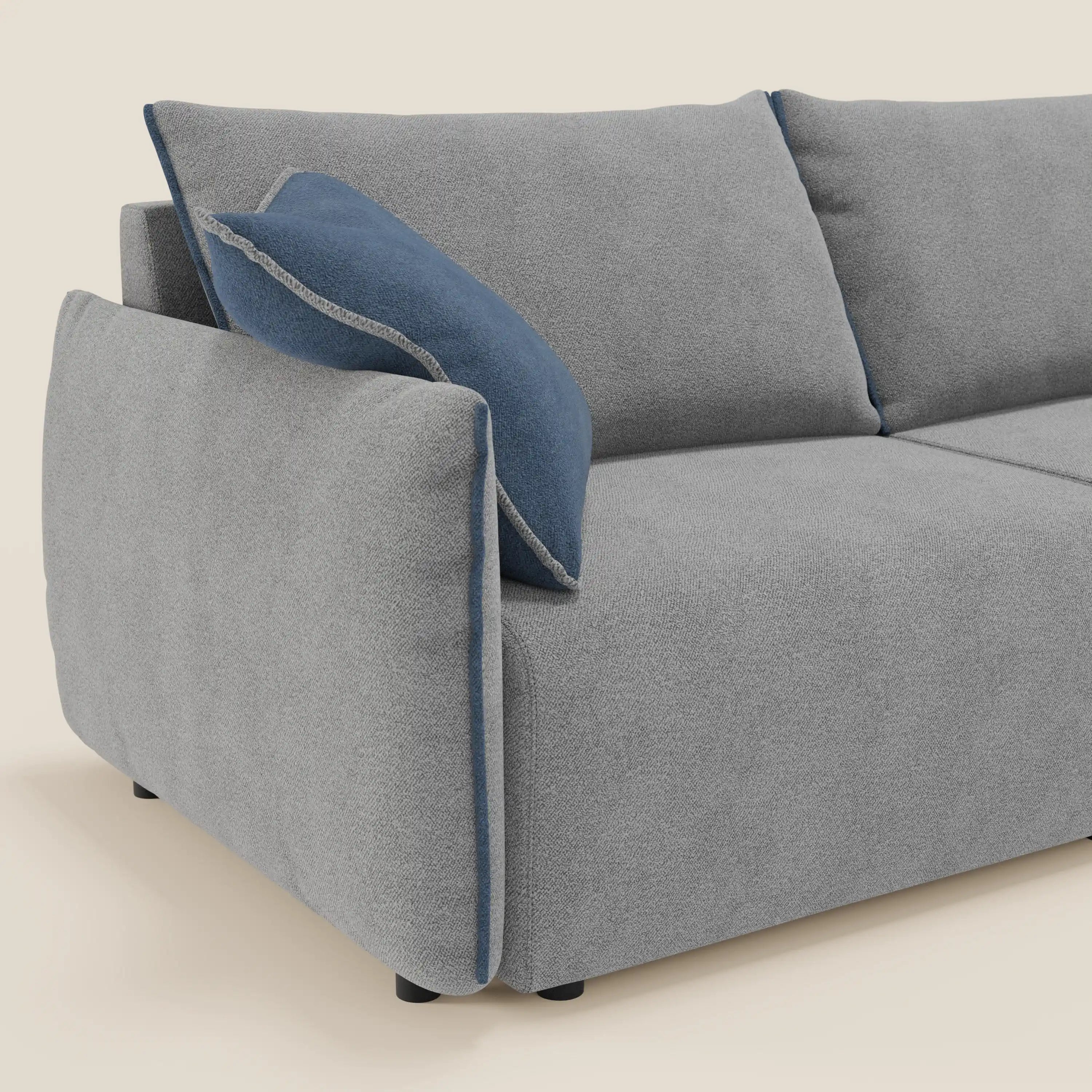 Il divano Flexar di Divani.Store con sedute allungabili e schienale in piuma è rivestito in morbido bouclé impermeabile T07 grigio-blu. Mostrato di lato, include un cuscino blu con bordo grigio e piedi neri contro sfondo beige.