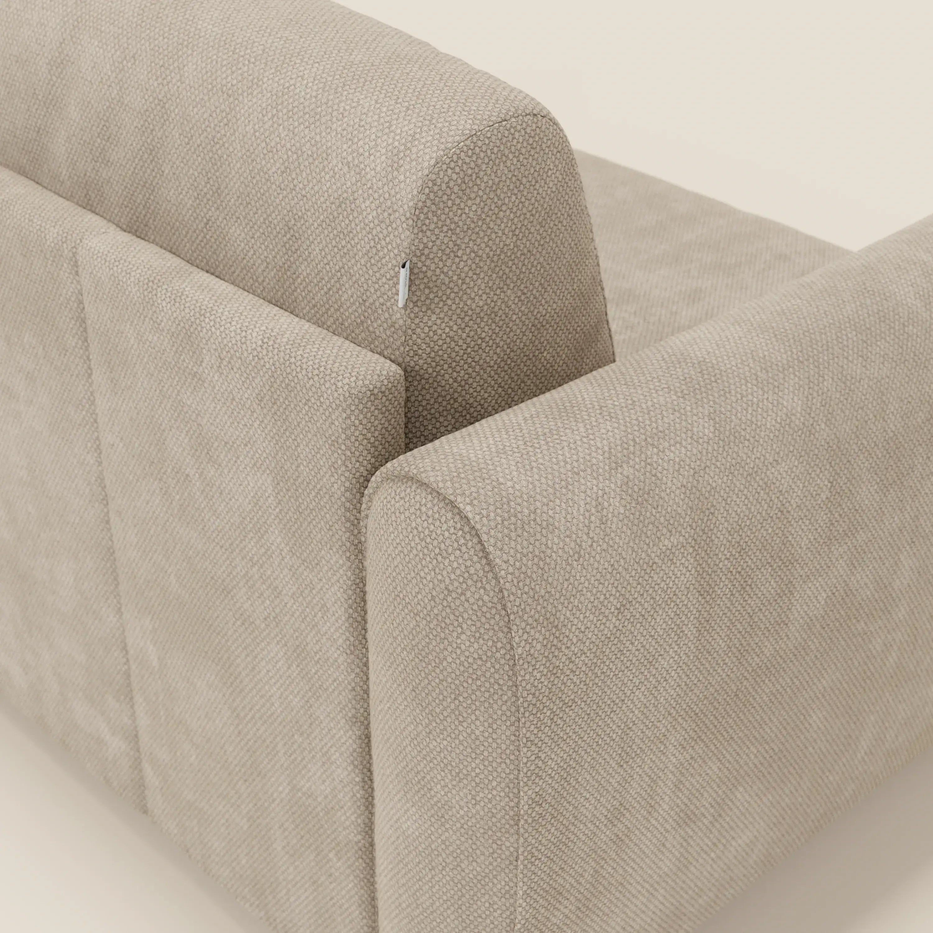 Un primo piano di Kaleo Divano letto moderno di Divani.Store in raffinato tessuto impermeabile T26 panna mostra l'imbottitura testurizzata, la cerniera posteriore superiore a vista, i bordi arrotondati e il design contemporaneo su uno sfondo chiaro.