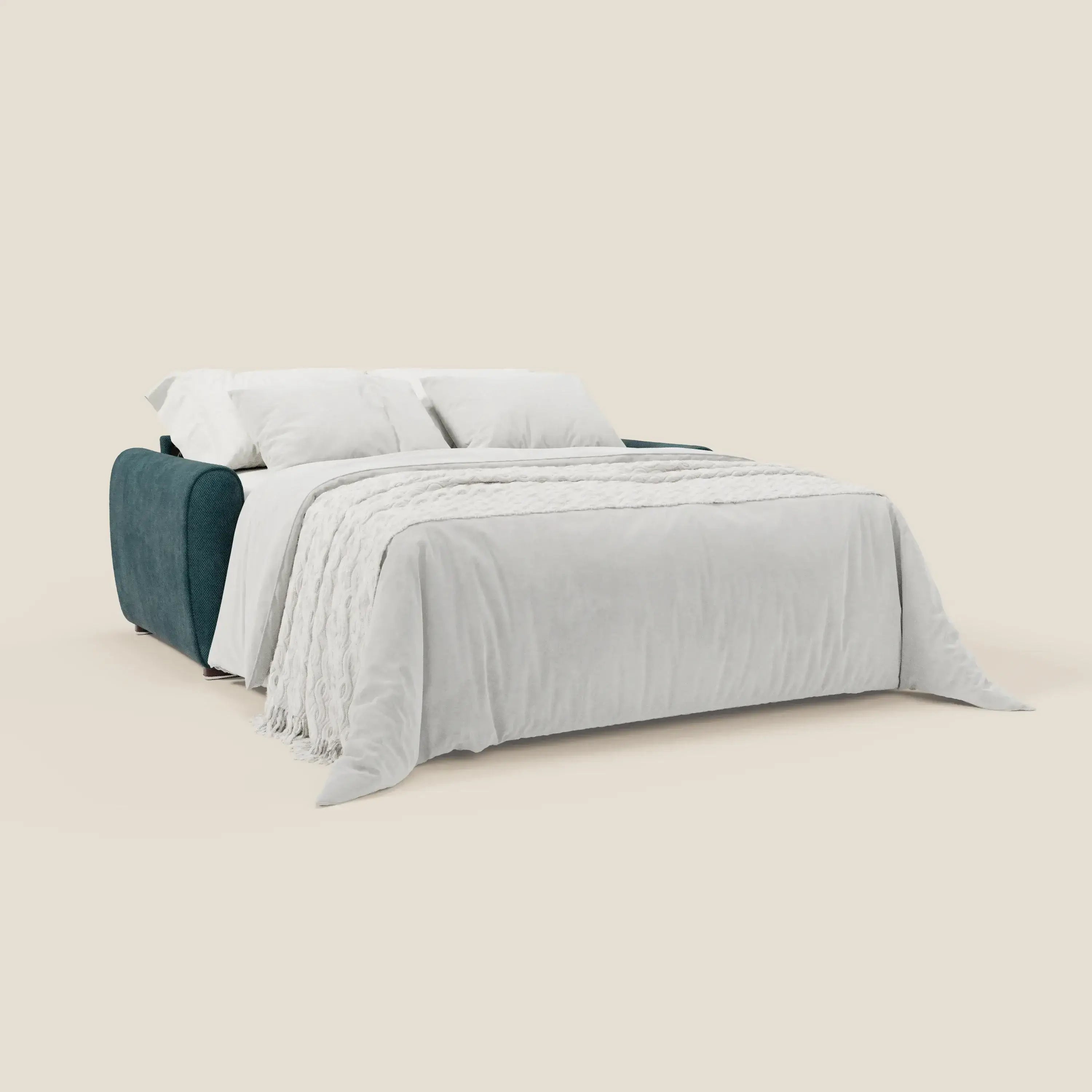 Il divano letto moderno Kaleo di Divani.Store in tessuto impermeabile T26 petrolio presenta un materasso H17 cm, coperta bianca, due cuscini bianchi e plaid con frange, su sfondo beige per uno stile contemporaneo.