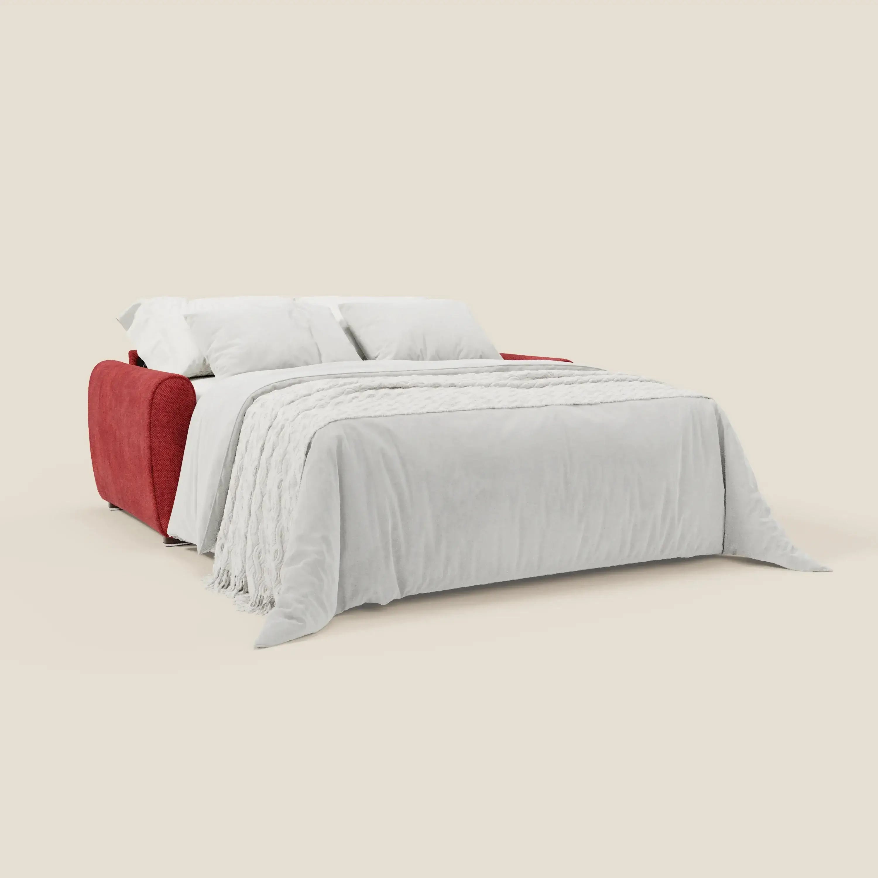 Il Kaleo Divano letto moderno con materasso H17 cm di Divani.Store è presentato dispiegato come un letto con un vivace tessuto impermeabile rosso T26, biancheria da letto bianca, due cuscini bianchi e una coperta con frange su sfondo beige.