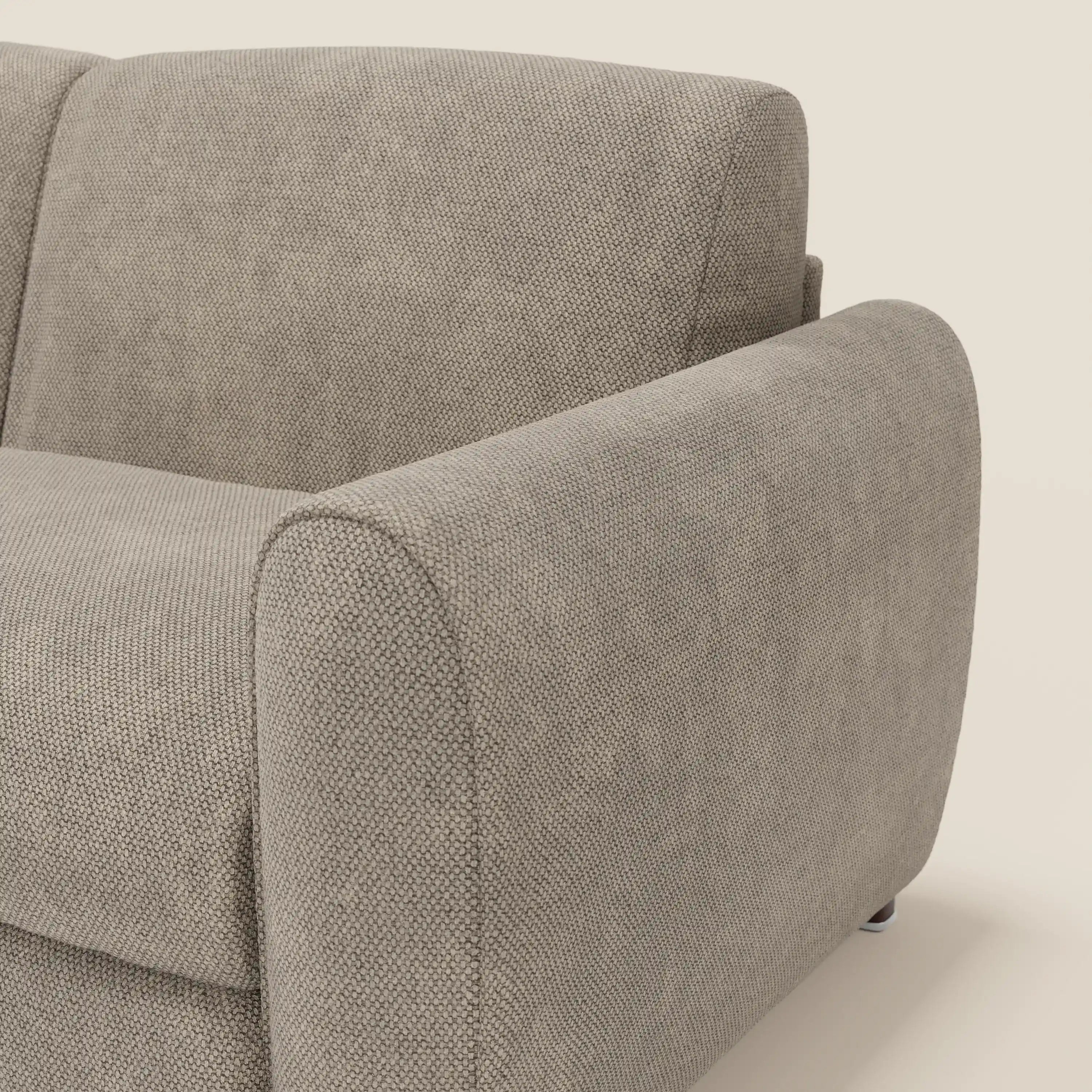 Primo piano del divano letto moderno Kaleo di Divani.Store, rivestito in raffinato tessuto impermeabile T26 tortora. L'immagine mostra l'ampio bracciolo e lo schienale imbottito con bordi morbidi e arrotondati su uno sfondo beige.