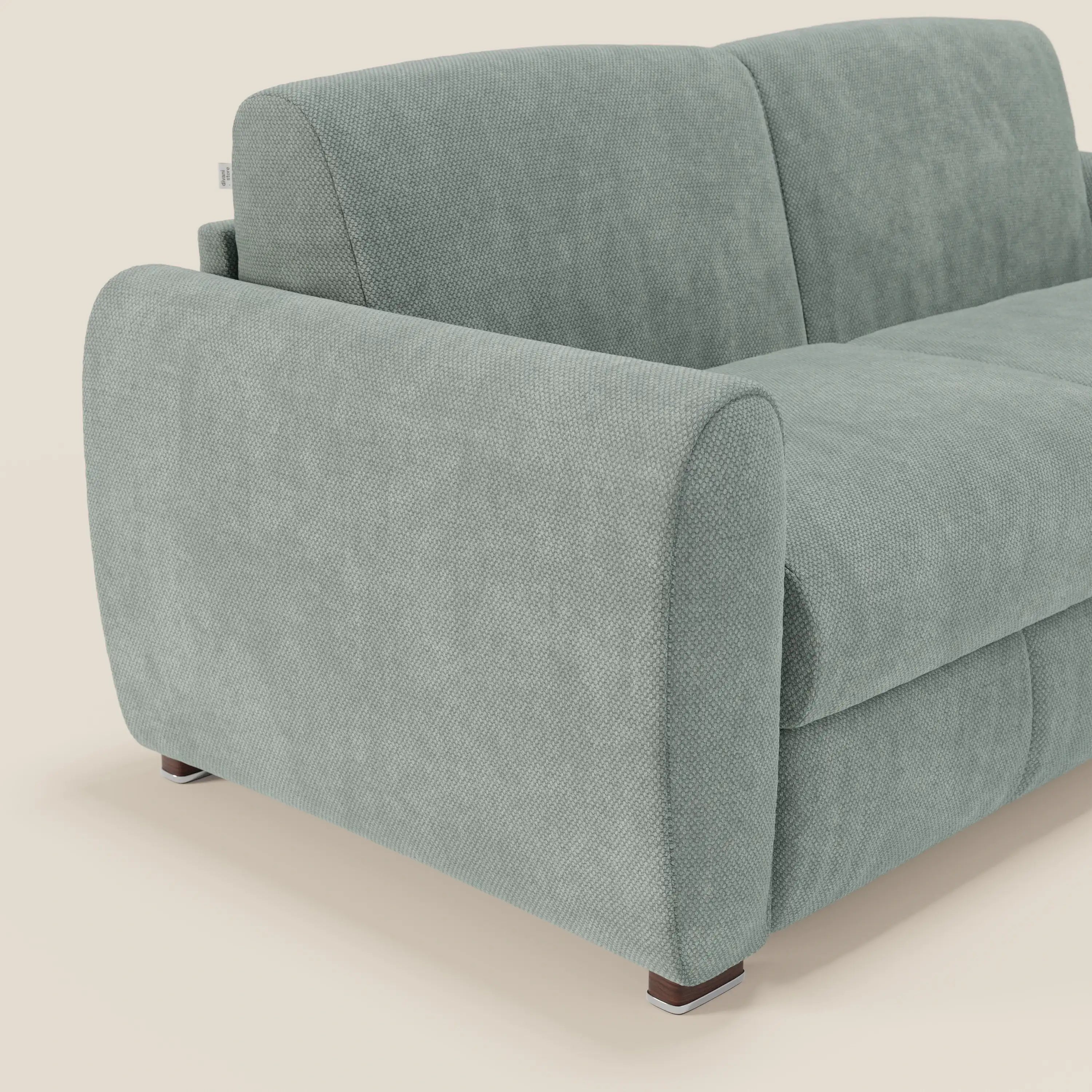 Il Kaleo Divano letto moderno di Divani.Store, in tessuto impermeabile T26 verde acqua, è caratterizzato da braccioli e schienali imbottiti e arrotondati e poggia su basse gambe in legno scuro con base bianca su sfondo chiaro.
