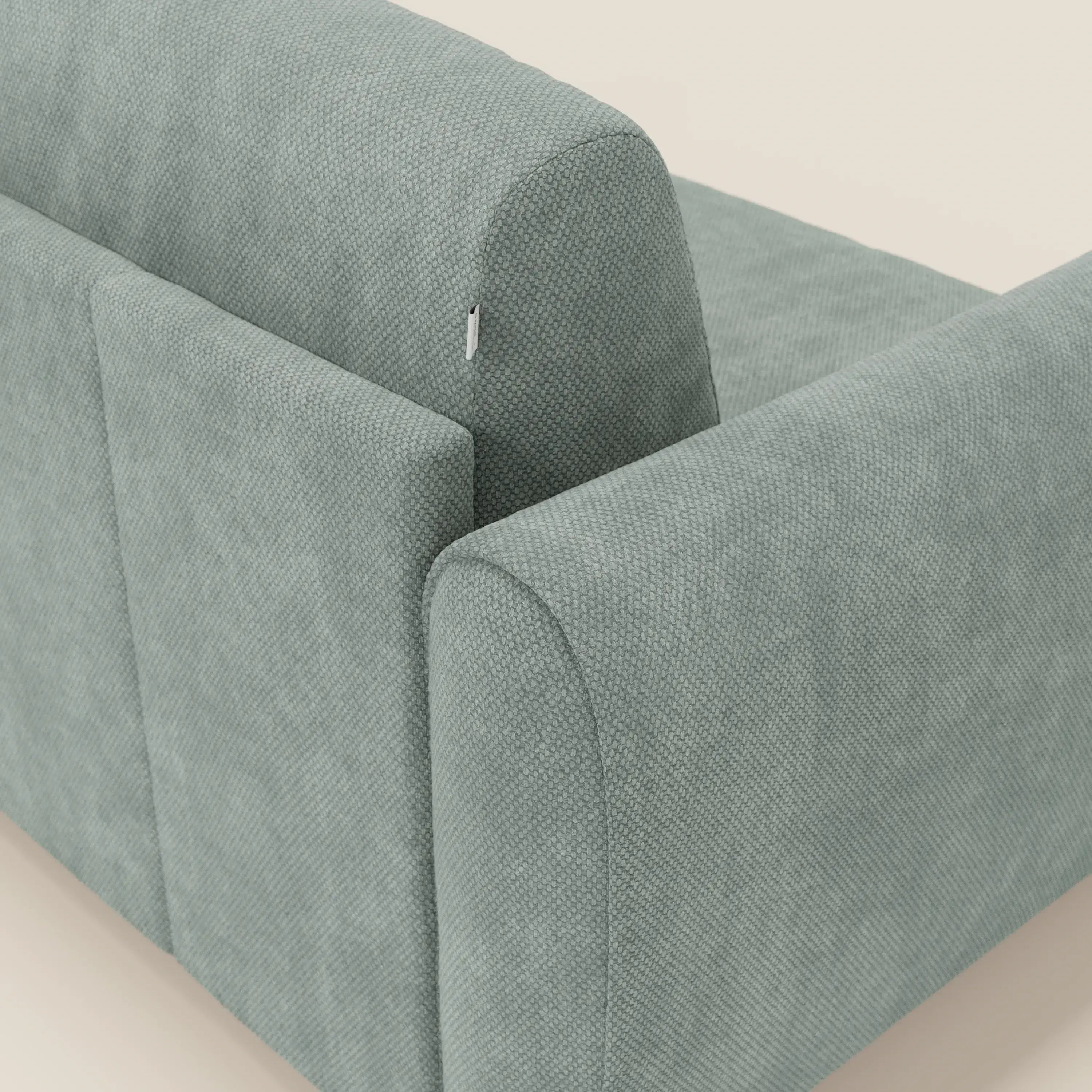 Un primo piano del Kaleo Divano letto moderno di Divani.Store in raffinato tessuto impermeabile T26 verde acqua mostra il cuscino di schienale sfoderabile con cerniera discreta, mettendo in evidenza il suo design contemporaneo su uno sfondo neutro.