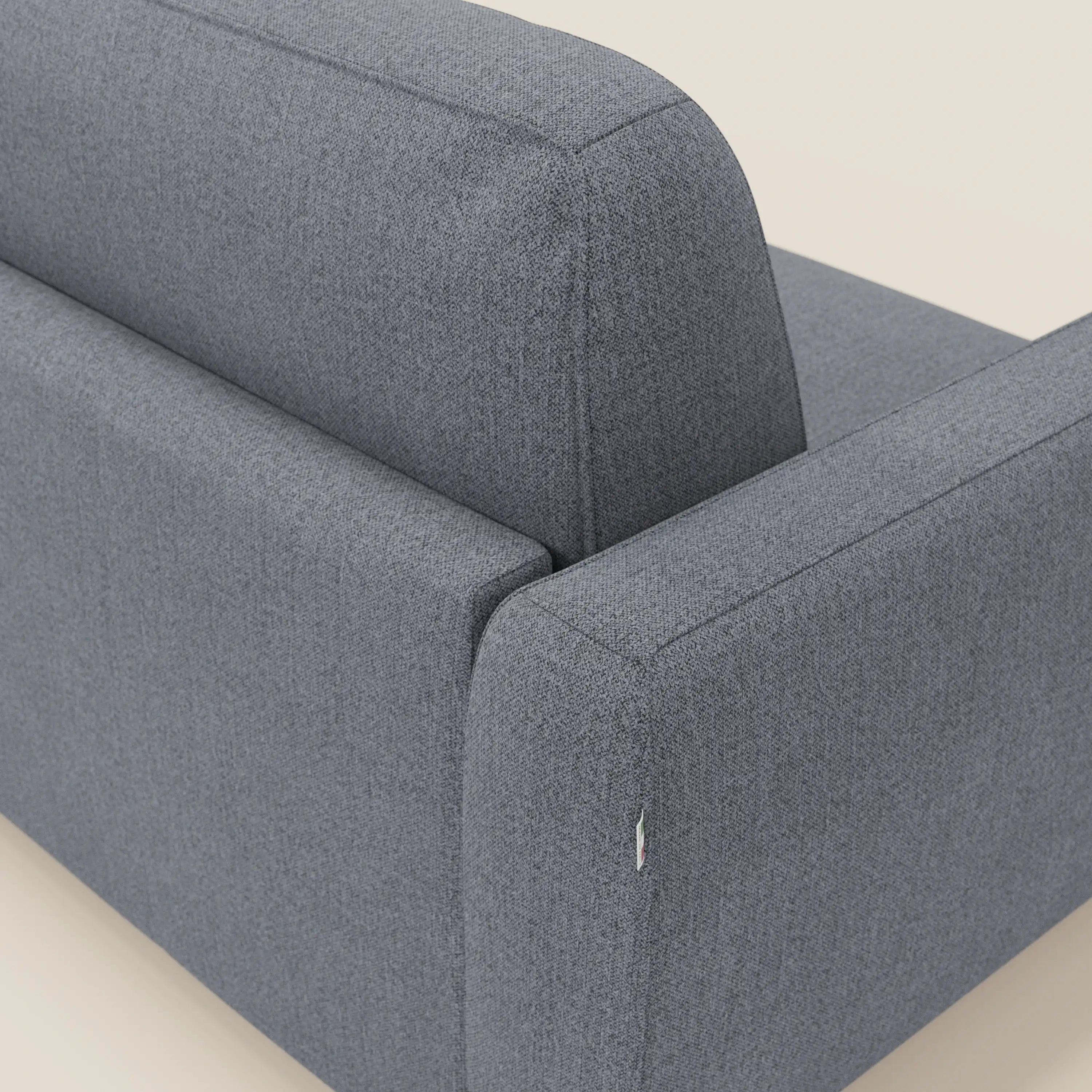 Un primo piano del divano letto sfoderabile Leonida di Divani.Store in Smacchiabile T23 blu grafite mostra le cuciture a vista e l'etichetta in tessuto sulla cucitura laterale, su un pavimento neutro bianco sporco. Include un materasso H18 cm e un vano porta guanciali.