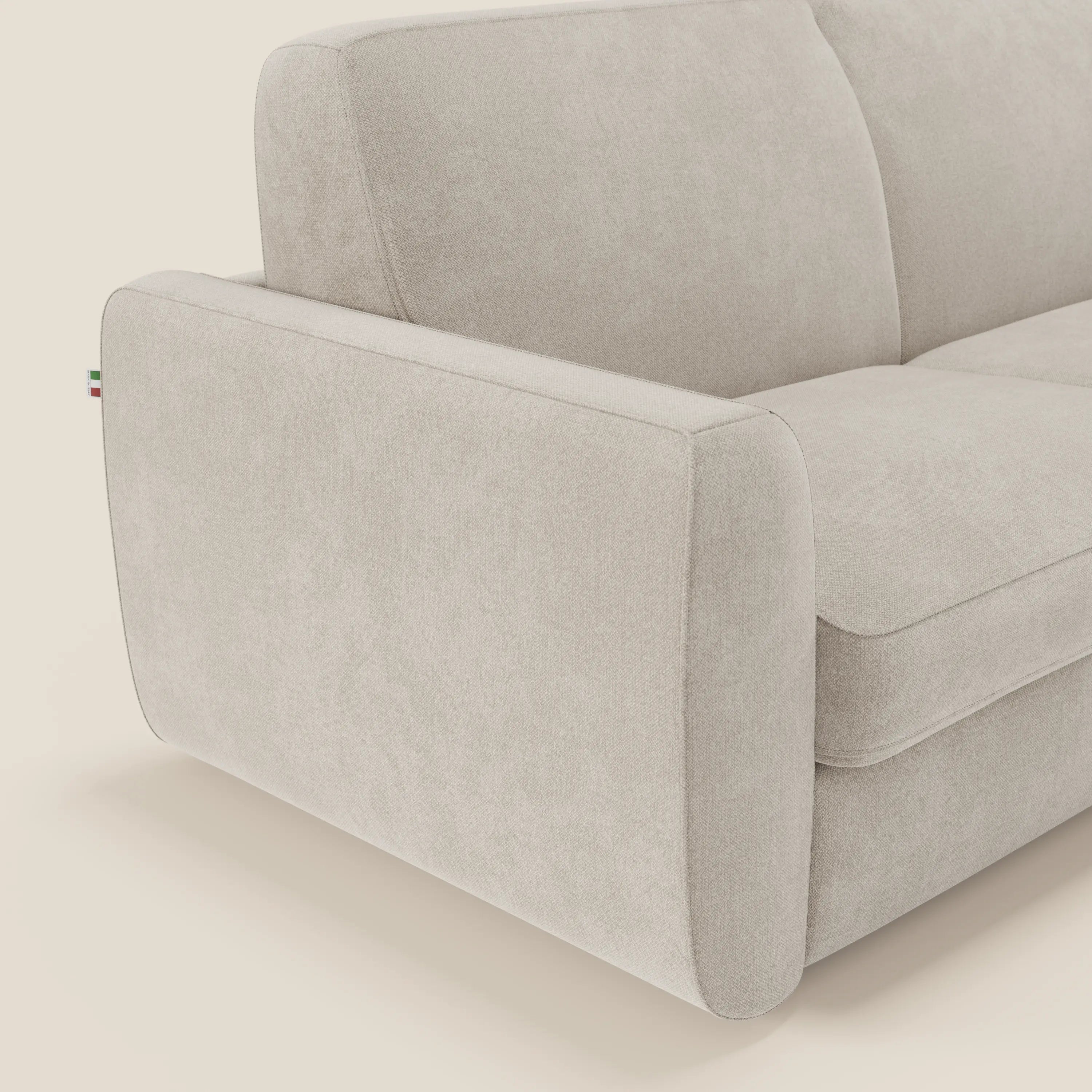 Un primo piano del divano letto sfoderabile Leonida di Divani.Store in tessuto smacchiabile T23 panna mostra i cuscini in tessuto, il bracciolo sinistro e la texture morbida, con una targhetta tricolore che sottolinea il meccanismo acciaio rinforzato.