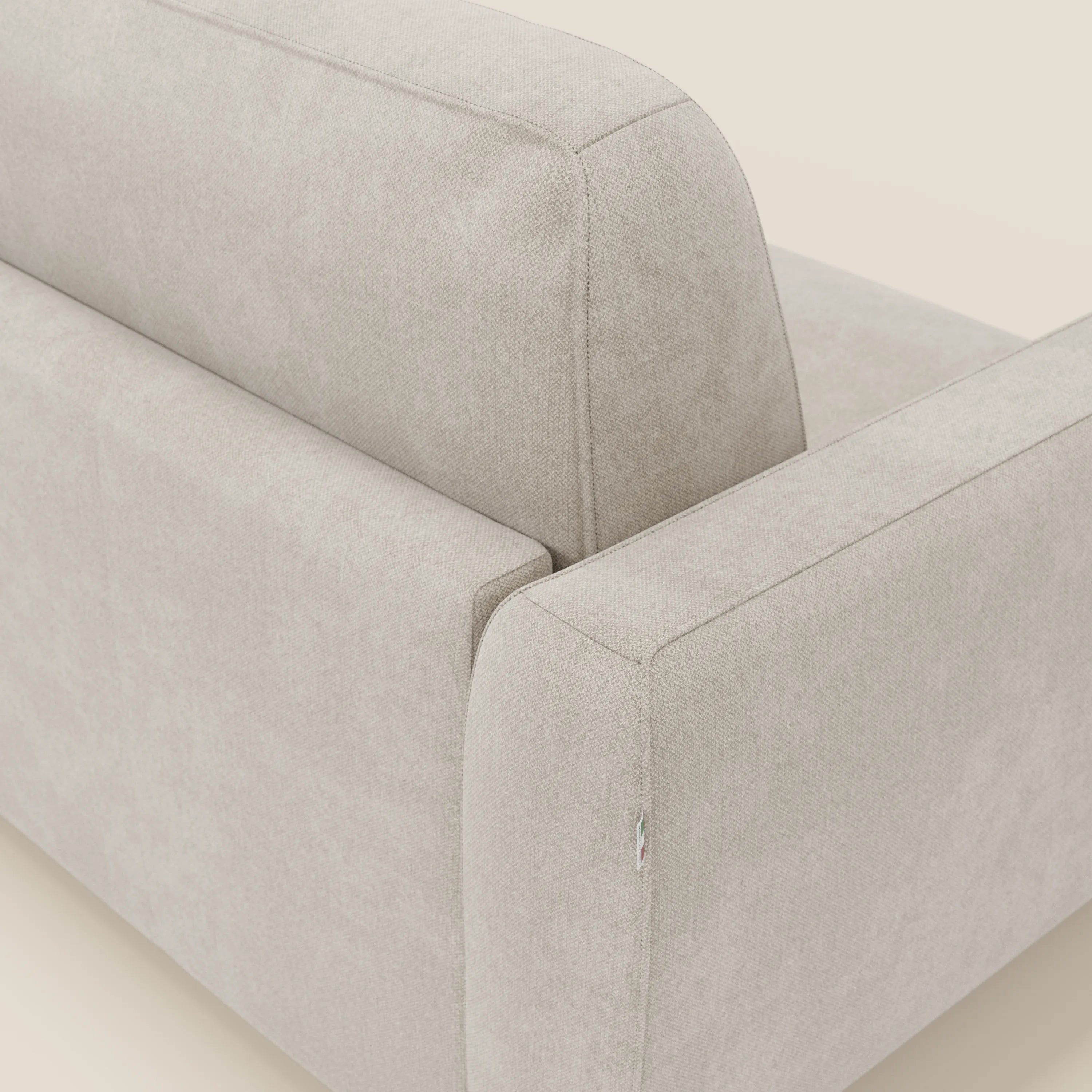 Un primo piano angolato del divano letto sfoderabile Leonida di Divani.Store in tessuto Smacchiabile T23 panna mostra il bracciolo, lo schienale e la seduta. Il tessuto morbido e strutturato e lo sfondo neutro ne evidenziano il design minimalista e moderno.