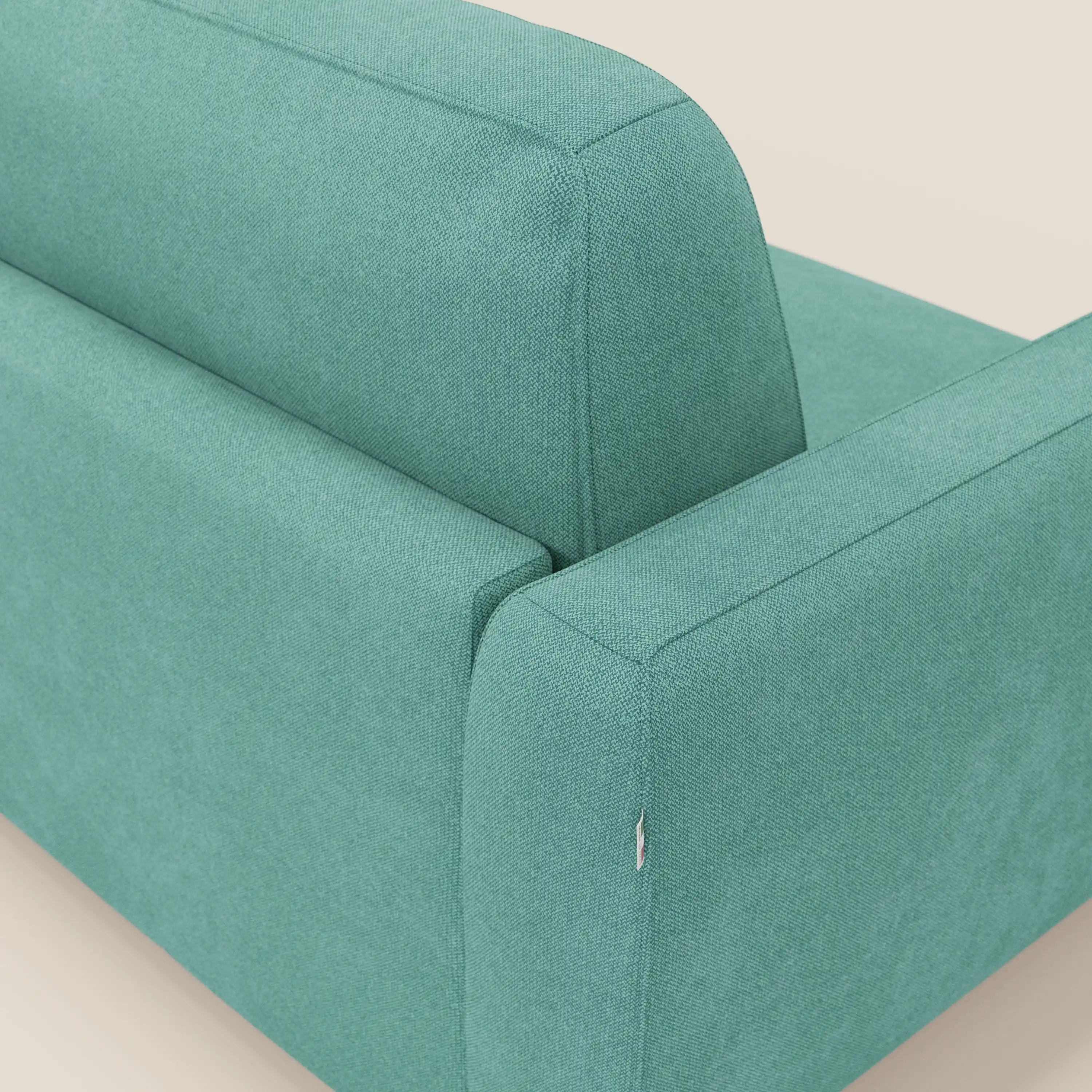 Un primo piano del divano letto sfoderabile Leonida di Divani.Store in smacchiabile T23 verde acqua, che mostra il tessuto strutturato, lo schienale e un bracciolo con un piccolo strappo vicino alla cucitura su uno sfondo bianco sporco.