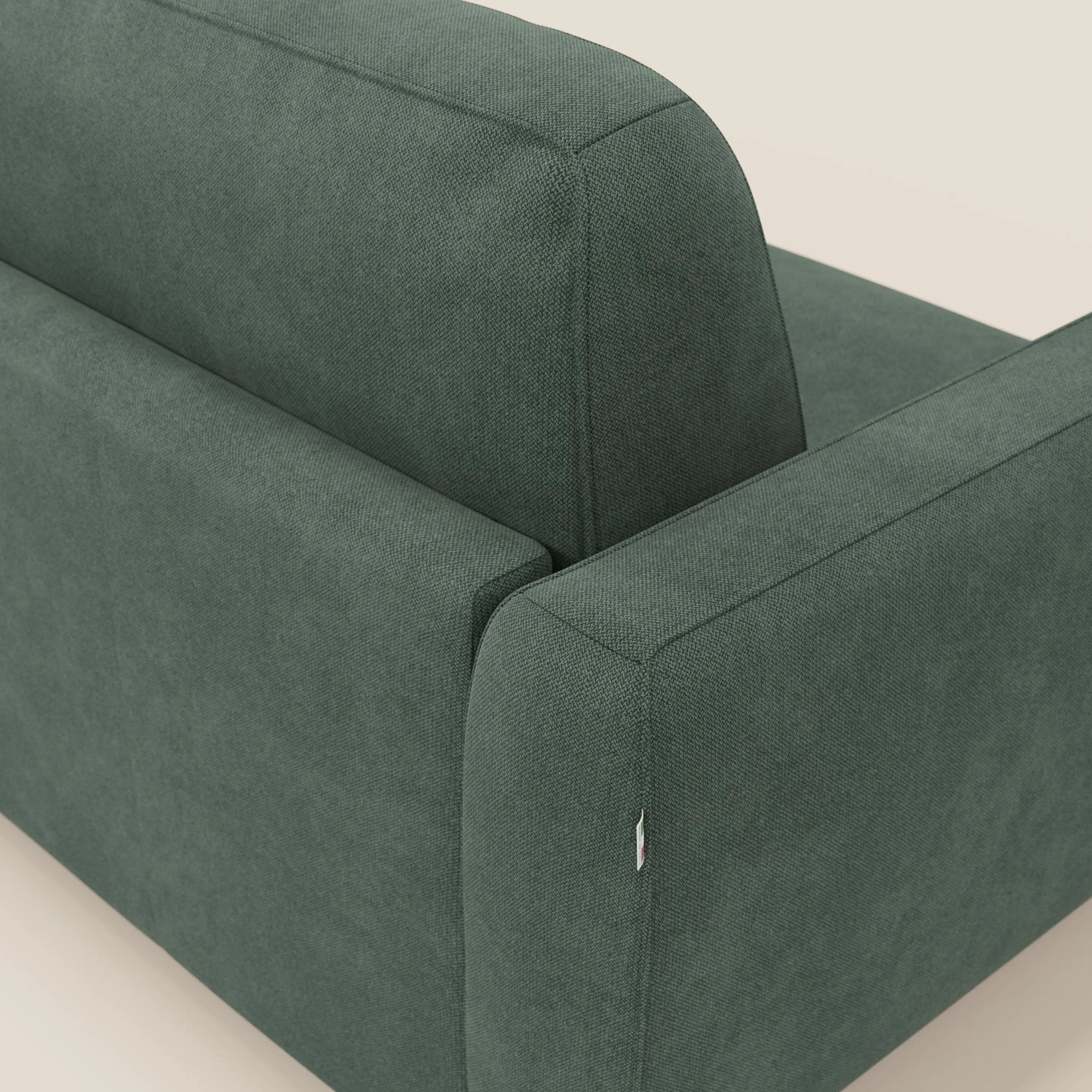 Primo piano dello schienale e del bracciolo del divano letto sfoderabile Leonida di Divani.Store, in tessuto smacchiabile T23 verde, dalle linee pulite e dalla texture morbida, su uno sfondo beige chiaro.