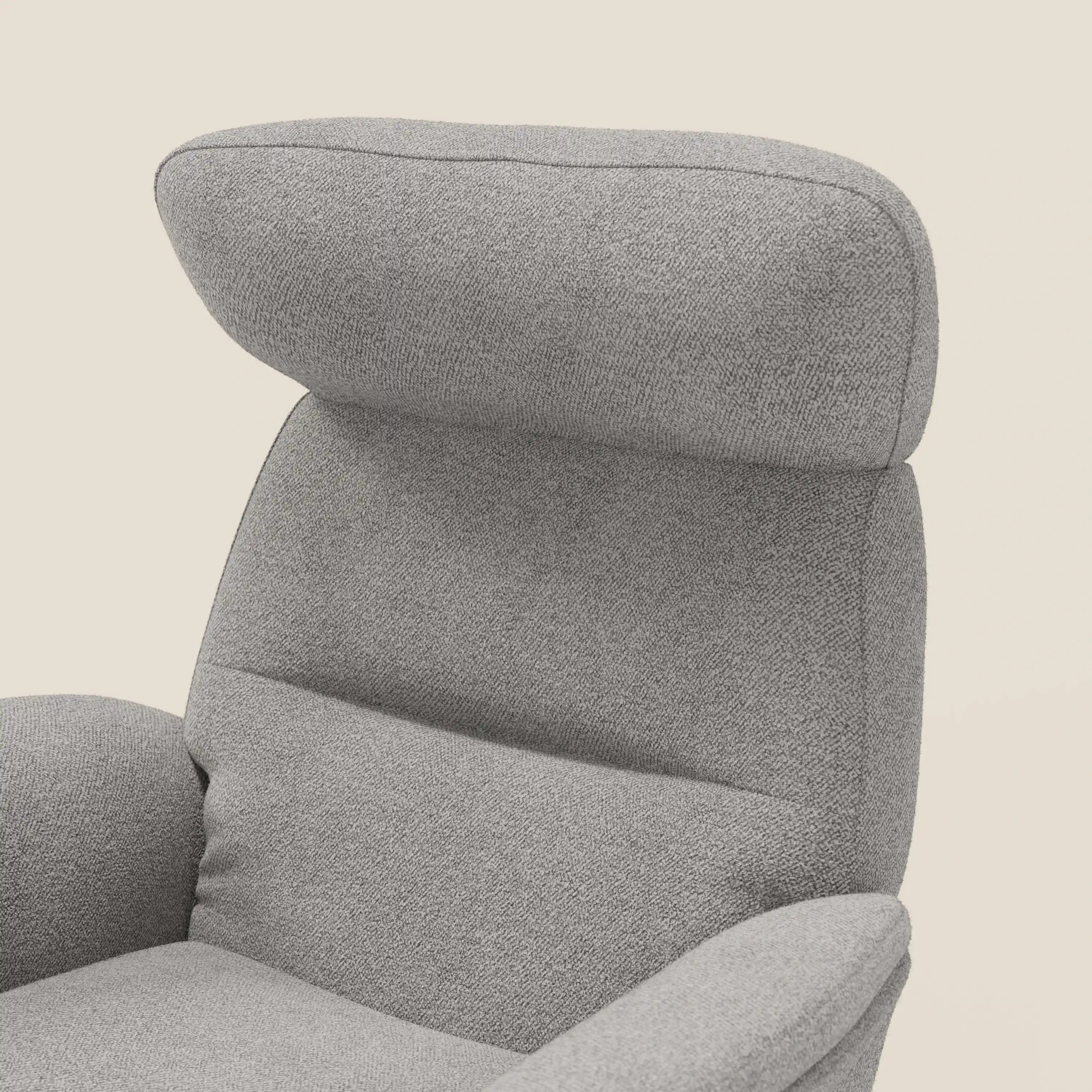Un primo piano della poltrona relax reclinabile Lunor di Divani.Store con pouf abbinato, rivestita in tessuto bouclé impermeabile grigio T07, caratterizzata da braccioli curvi, poggiatesta imbottito e schienale alto per garantire comfort e stile su uno sfondo bianco sporco.