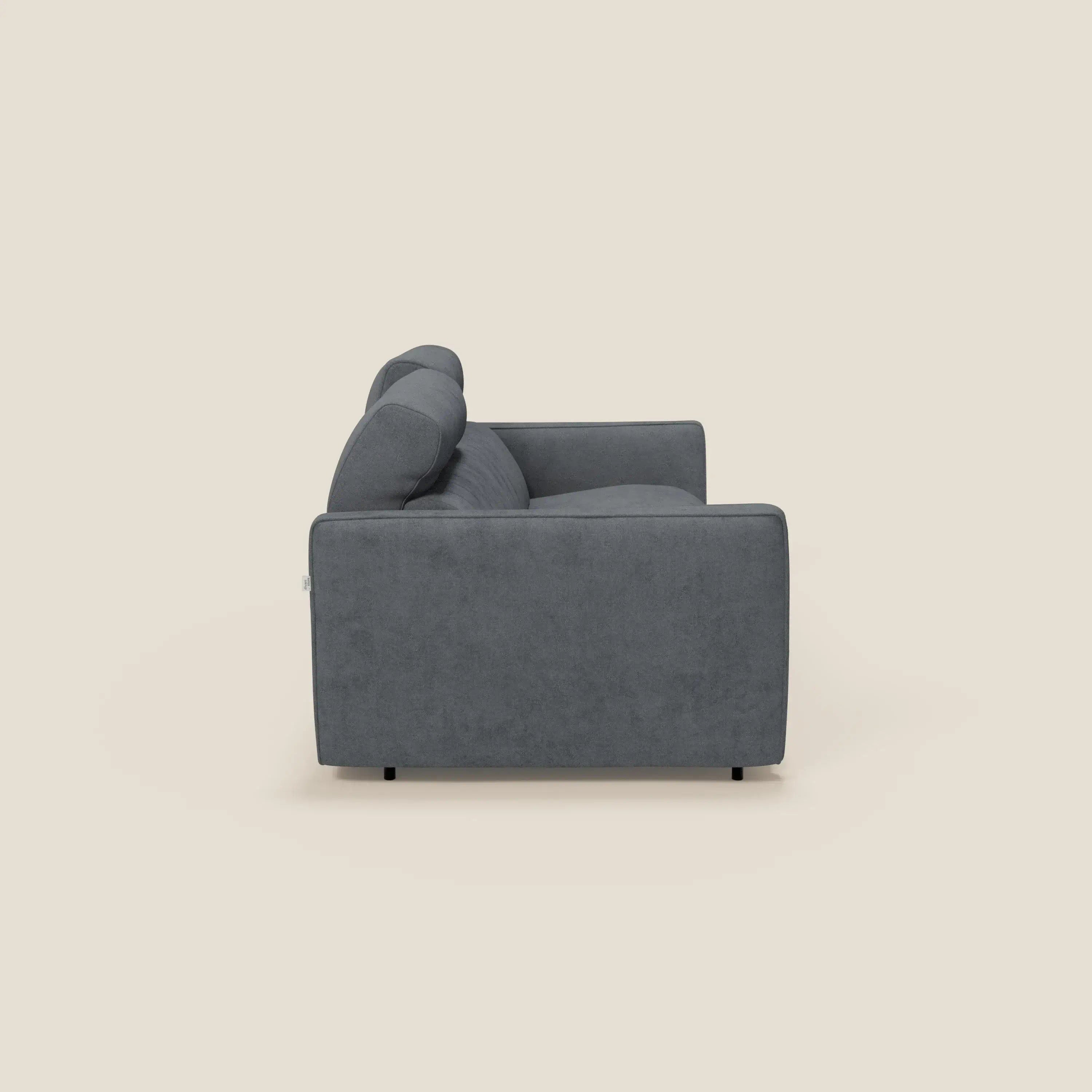 Vista laterale del divano letto moderno Nivon di Divani.Store, con materasso H16 cm, poggiatesta e tessuto impermeabile T25 grigio scuro. Questo divano squadrato con cuscini e gambe corte di colore nero è inserito in uno sfondo beige chiaro.