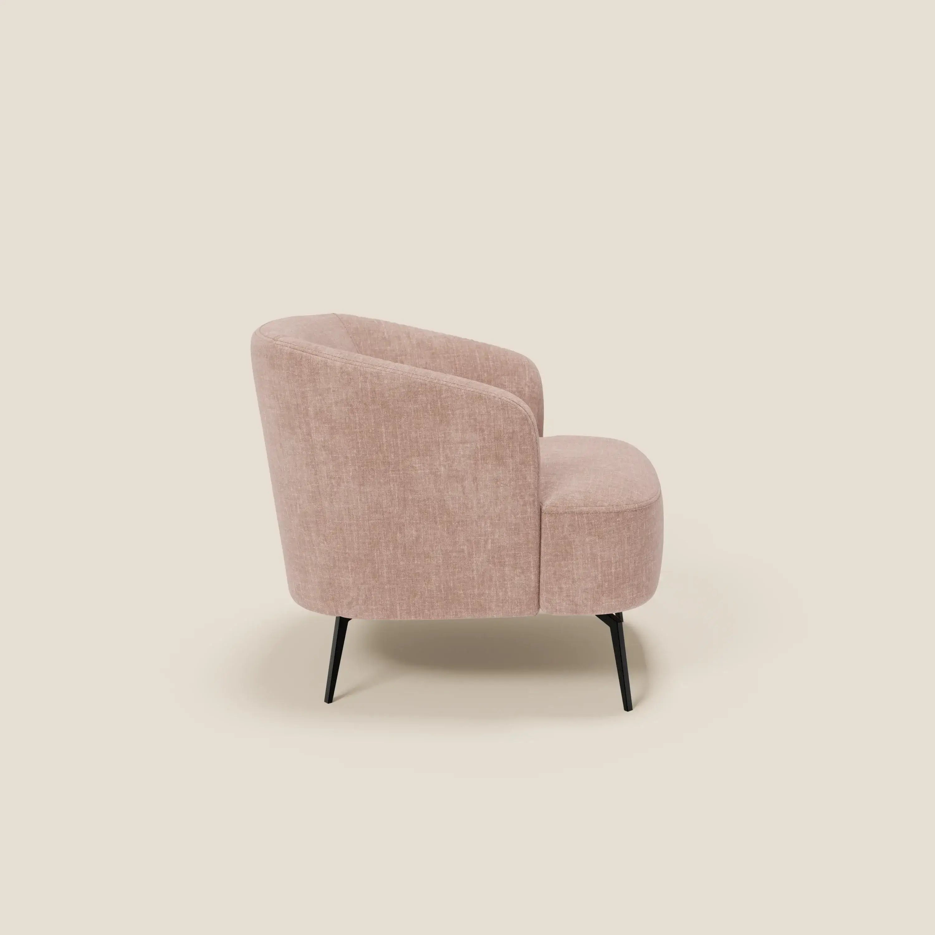 La poltroncina Renoa di Divani.Store è caratterizzata da un moderno tessuto smacchiabile T24 rosa blush, schienale e fianchi arrotondati e quattro sottili gambe in metallo nero. Vista di lato su uno sfondo beige chiaro.
