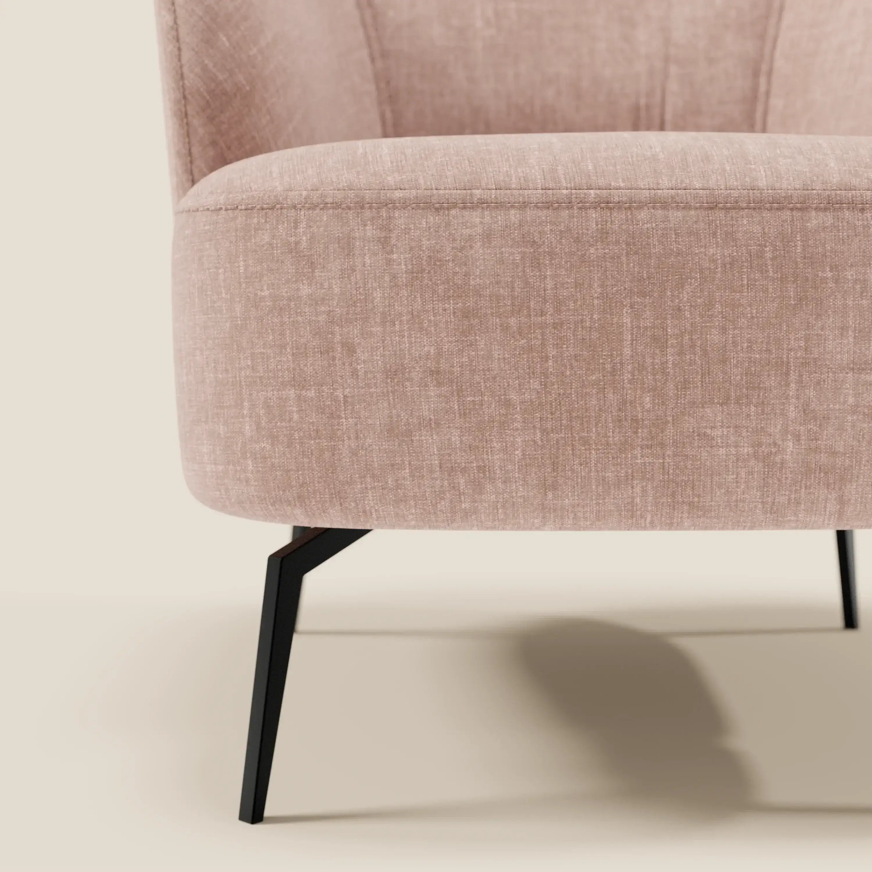 Primo piano della poltroncina Renoa dall'eleganza moderna di Divani.Store, rivestita in morbido tessuto T24 rosa cipria smacchiabile, con sottili gambe in metallo nero e design curvo. Solo una parte della sedia è visibile su uno sfondo beige.