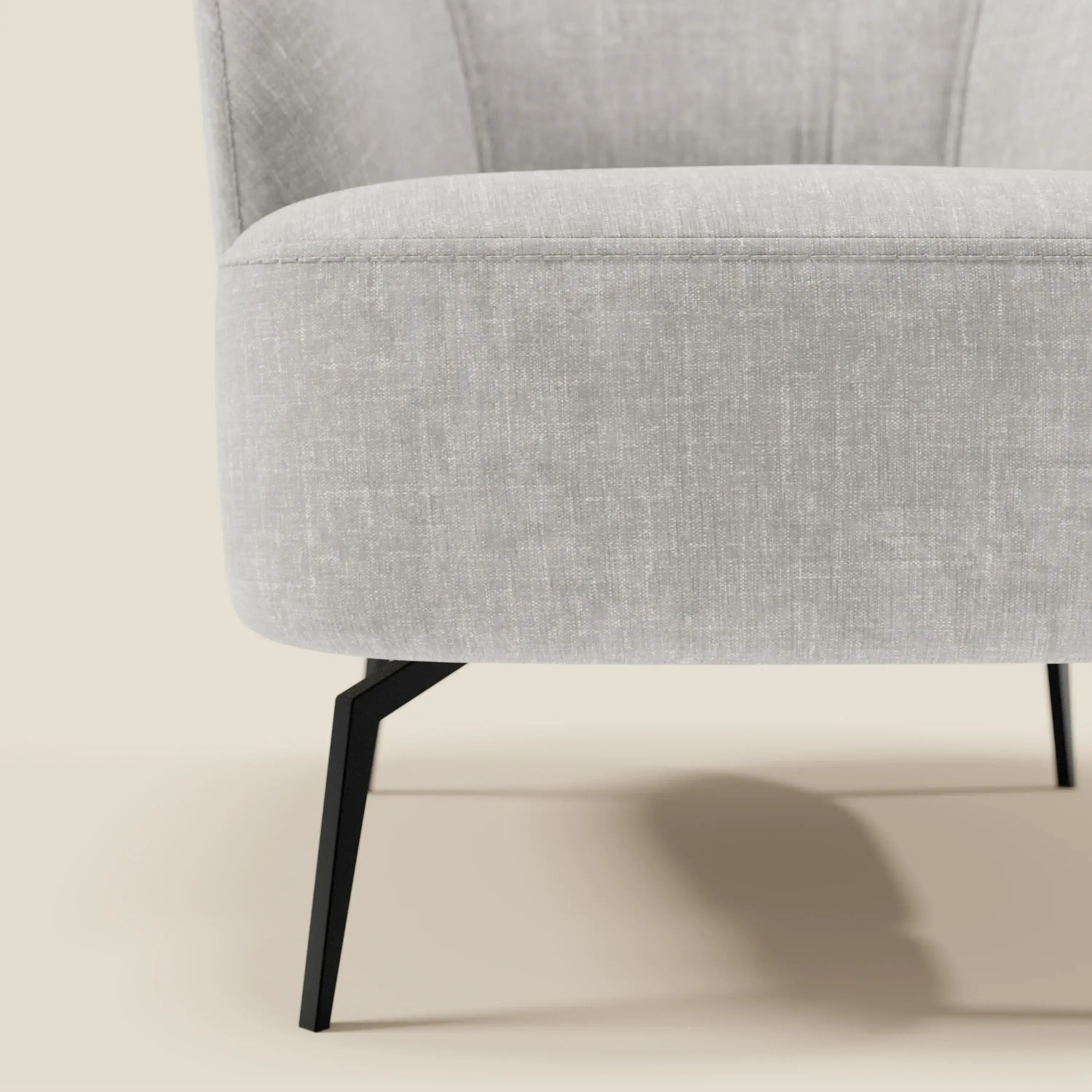 Primo piano della poltroncina Renoa di Divani.Store, caratterizzata da un'eleganza moderna con tessuto smacchiabile T24 grigio chiaro, eleganti gambe in metallo nero e una seduta/schienale morbidamente curvata per un comfort avvolgente su uno sfondo beige neutro.