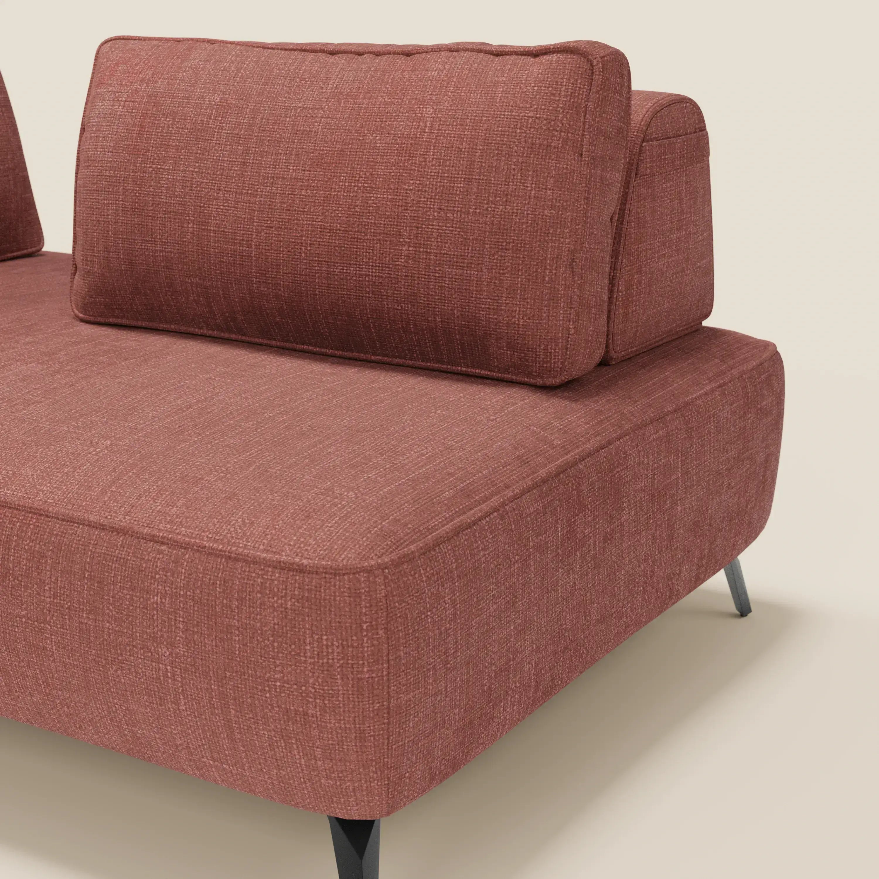 Un primo piano del divano modulare Volta di Divani.Store in raffinato tessuto ciniglia T06 corallo, con mobili schienali, uno spesso cuscino di seduta e gambe angolari nere su uno sfondo beige chiaro.