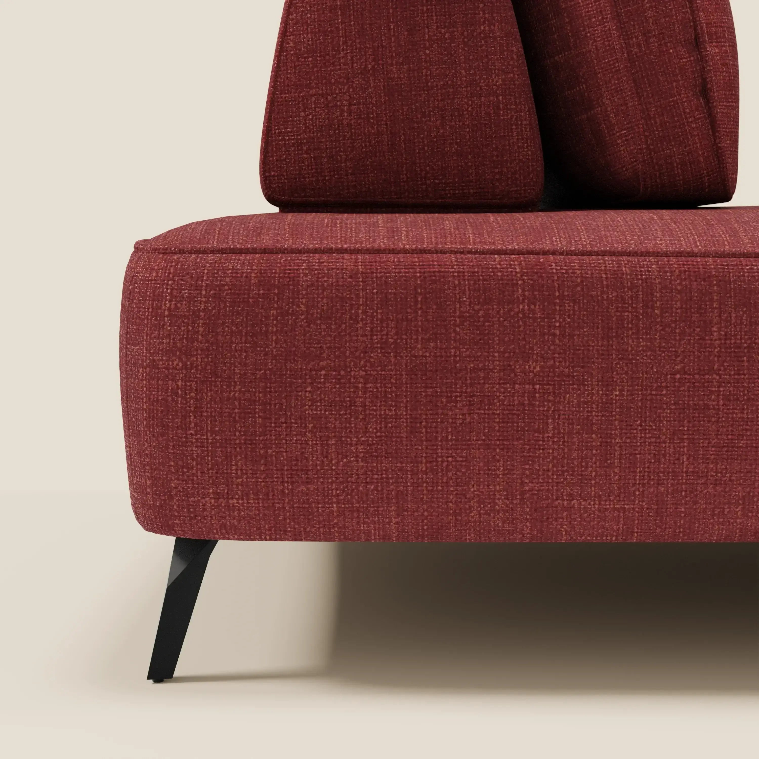 Primo piano del divano modulare Volta di Divani.Store, con schienale mobile e raffinato tessuto in ciniglia rossa T06. La gamba e la base in metallo a vista e i due cuscini coordinati contrastano con una parete e un pavimento in bianco sporco.