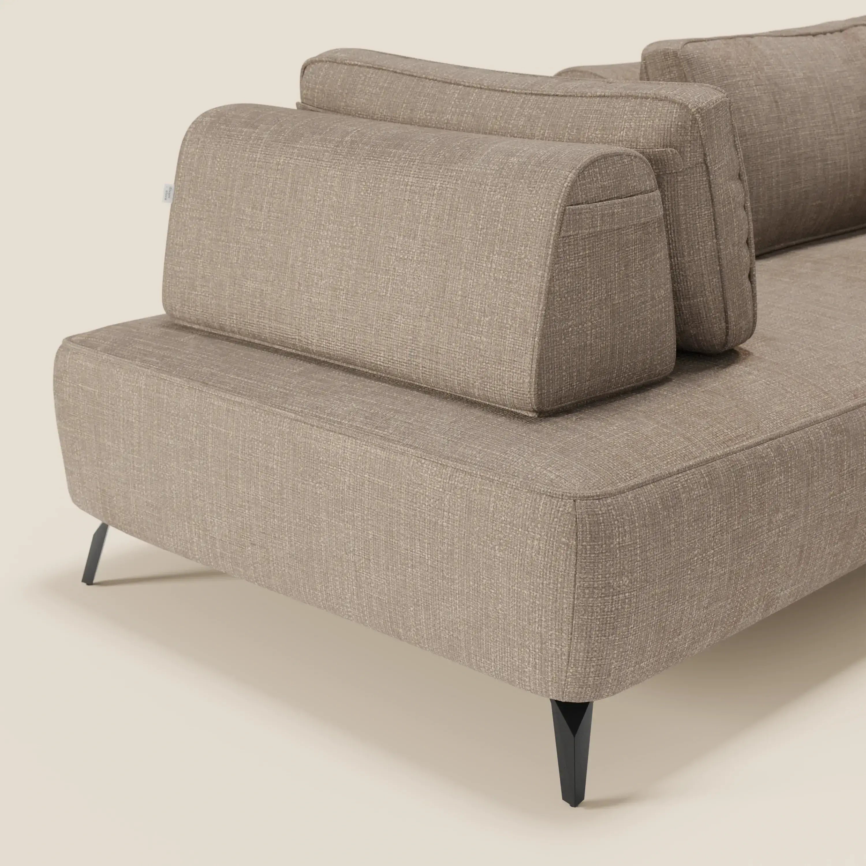 Primo piano di Volta divano modulare con schienali mobili in raffinato tessuto ciniglia T06 tortora di Divani.Store, caratterizzato da gambe in metallo angolate nere e cuscini dello schienale in feltro. Lo sfondo beige in tinta unita ne evidenzia le linee pulite e il design contemporaneo.