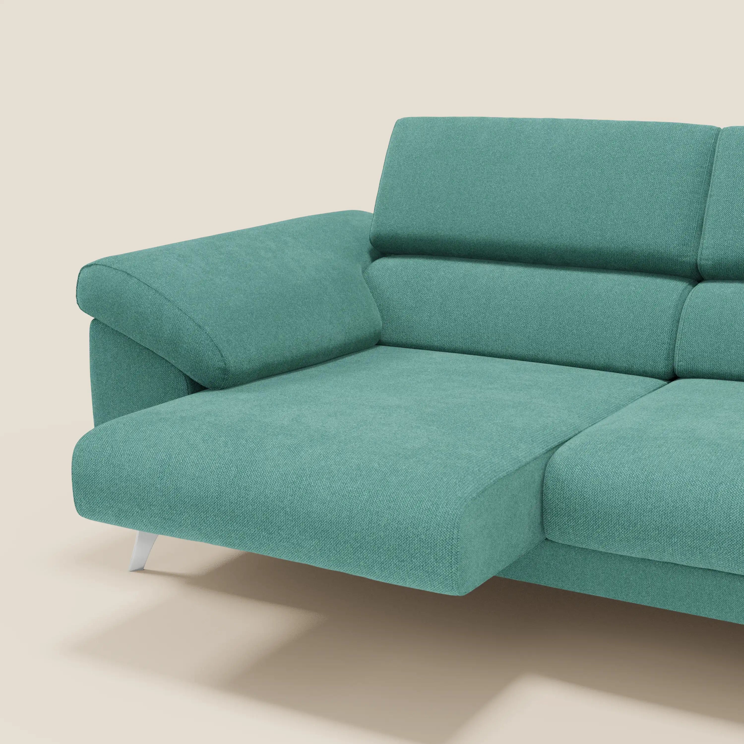 Il divano Donatello di Divani.Store, in tessuto verde acqua T23, facile da pulire, è caratterizzato da sedute allungabili, braccioli contenitori e poggiatesta reclinabili: un moderno divano italiano con chaise longue a sinistra, su uno sfondo beige chiaro.