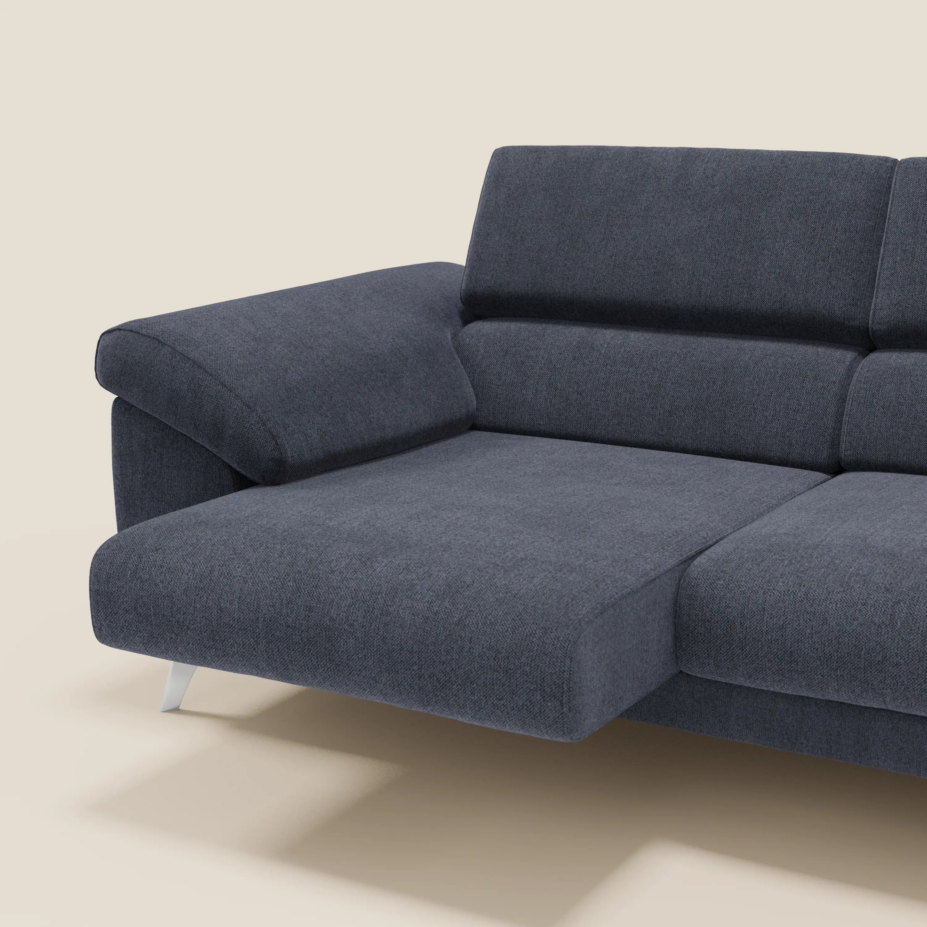 Il divano componibile Donatello di Divani.Store, in tessuto antimacchia T23 blu ardesia, è caratterizzato da sedute allungabili, braccioli contenitori e poggiatesta regolabili. Presentato su sfondo beige con una chaise allungata ed eleganti gambe in metallo.