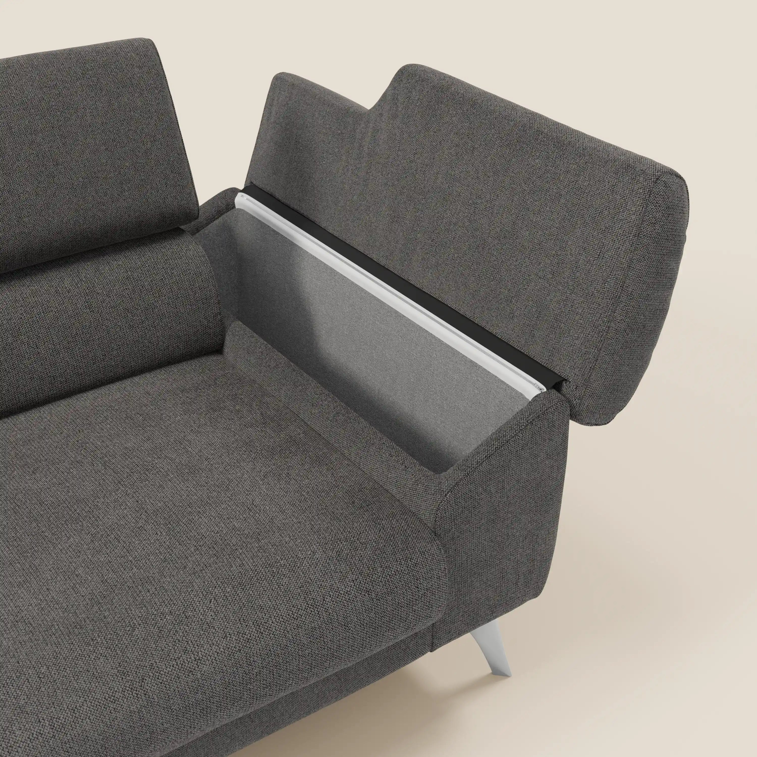 Il divano Donatello di Divani.Store in tessuto lavabile T23 antracite è caratterizzato da sedute allungabili, braccioli contenitori e poggiatesta reclinabili. Il suo design moderno poggia su eleganti gambe chiare su uno sfondo color crema.