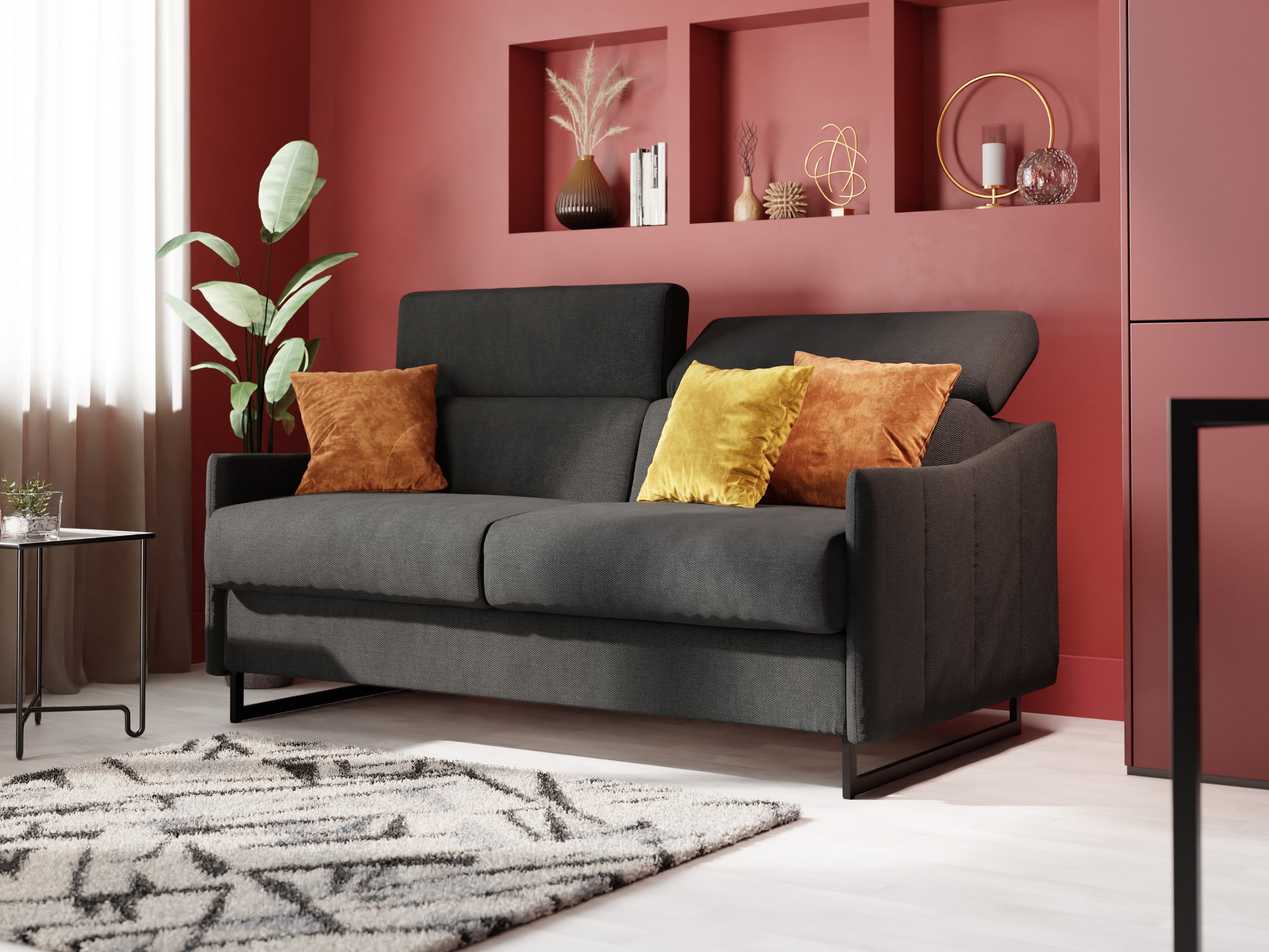 Camera da letto moderna con divano letto grigio, lenzuola bianche e una coperta grigia. Due stampe botaniche incorniciate sono appese sopra. Ampia finestra, pareti chiare, pavimento in legno, tavolino con vaso e arredamento accogliente.
