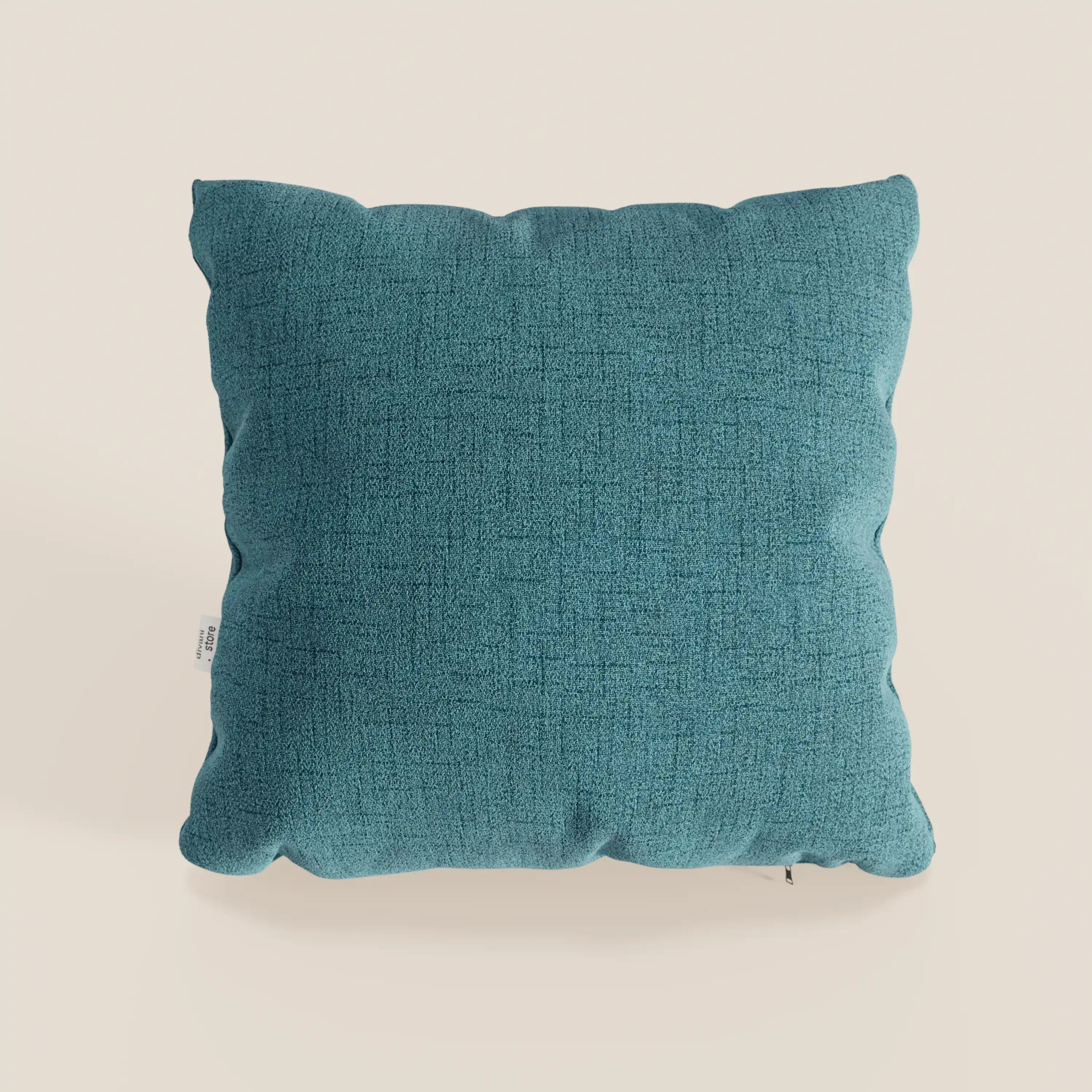 Un cuscino Felis quadrato di Divani.Store in tessuto impermeabile azzurro T03 con superficie testurizzata è centrato su uno sfondo crema chiaro, con angoli arrotondati, cuciture a vista e una piccola etichetta sul bordo sinistro.