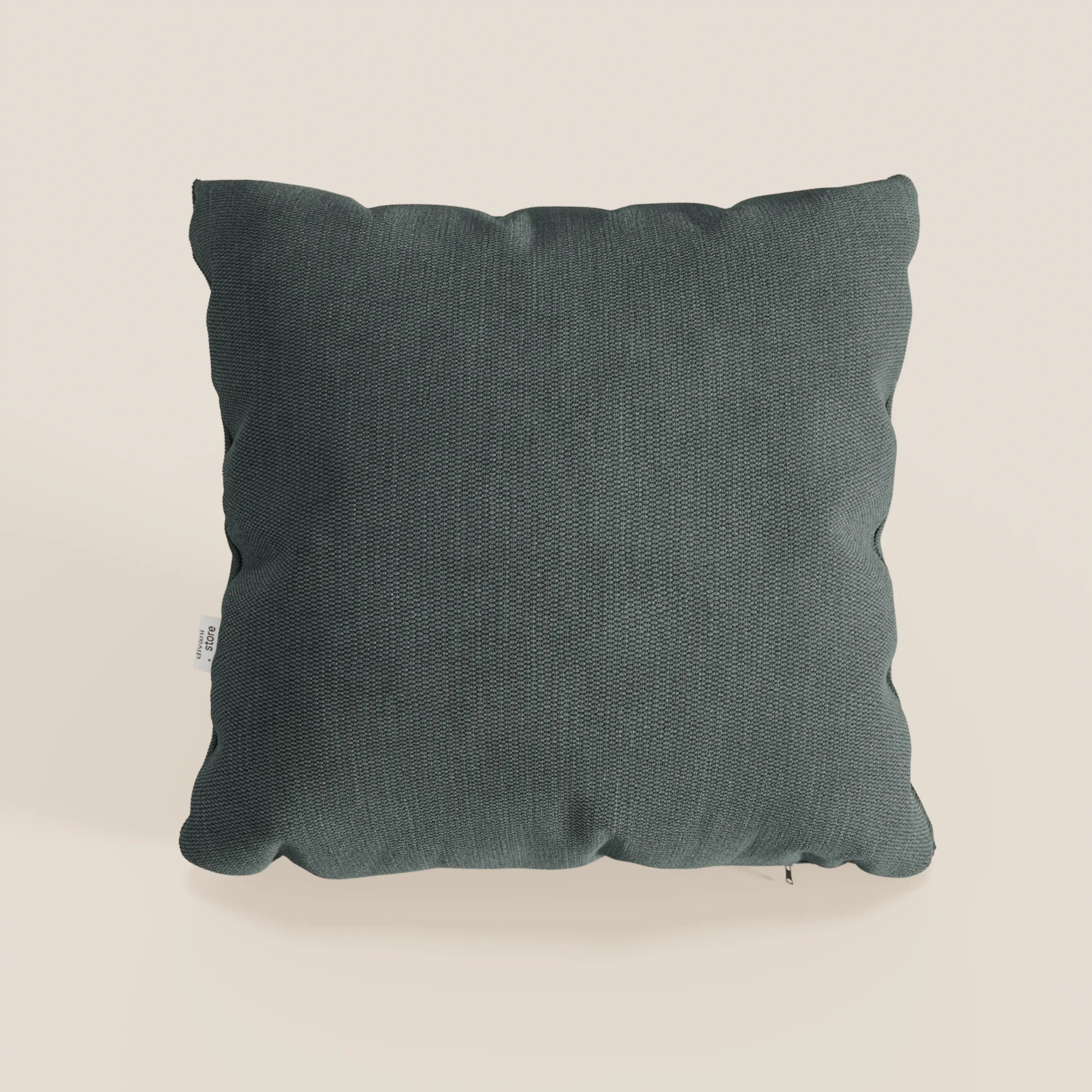 Un cuscino quadrato Miami 45x45 cm in morbido tessuto impermeabile T14 verde di Divani.Store è centrato su un fondo beige chiaro, felpato e leggermente stropicciato, con una piccola etichetta bianca sulla cucitura sinistra.
