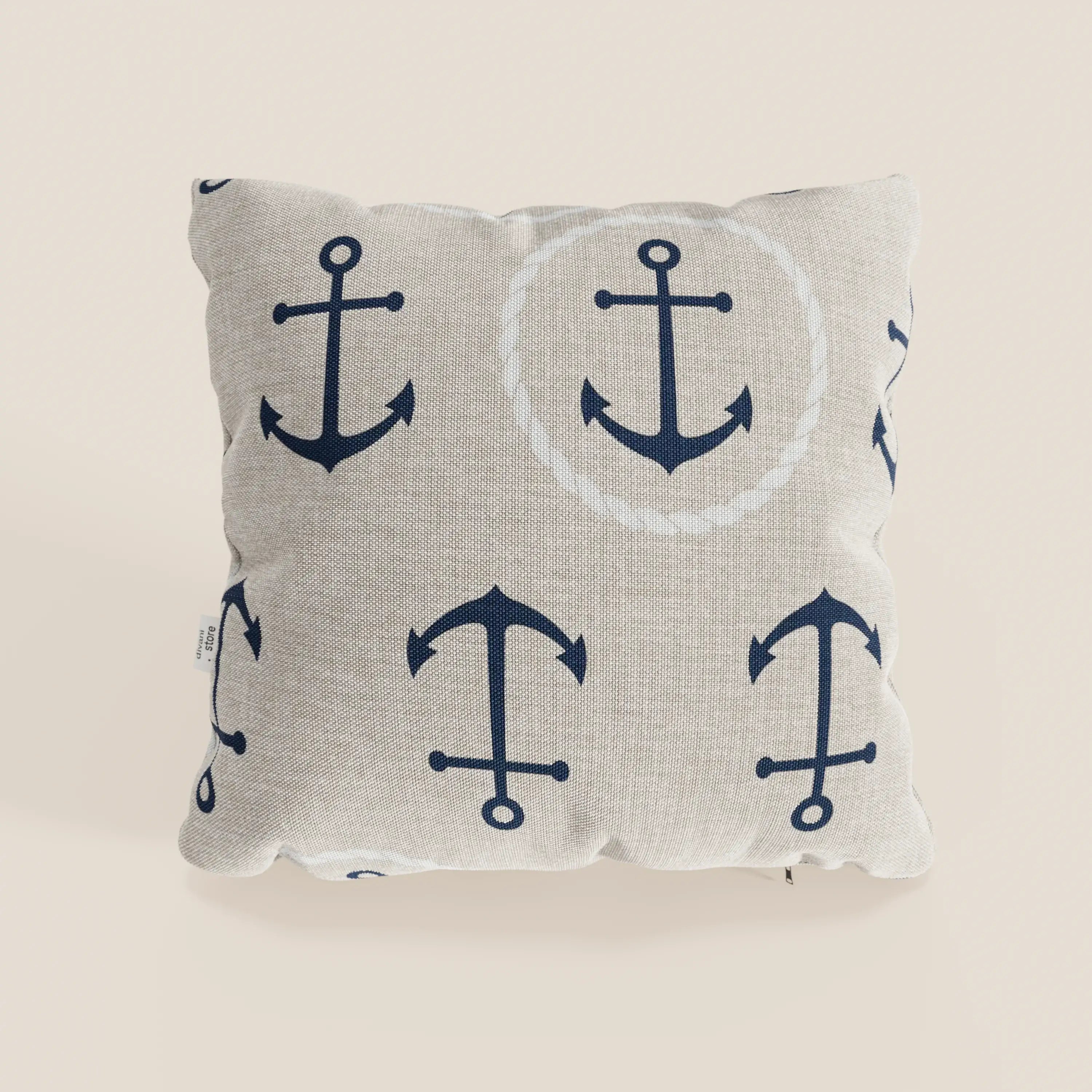 La collezione di cuscini Nautilus di Divani.Store presenta un cuscino quadrato beige in tessuto impermeabile, con ancore nautiche blu scuro, una delle quali incorniciata da una corda bianca, per un arredamento marino di stile. Esposto su uno sfondo semplice e chiaro.