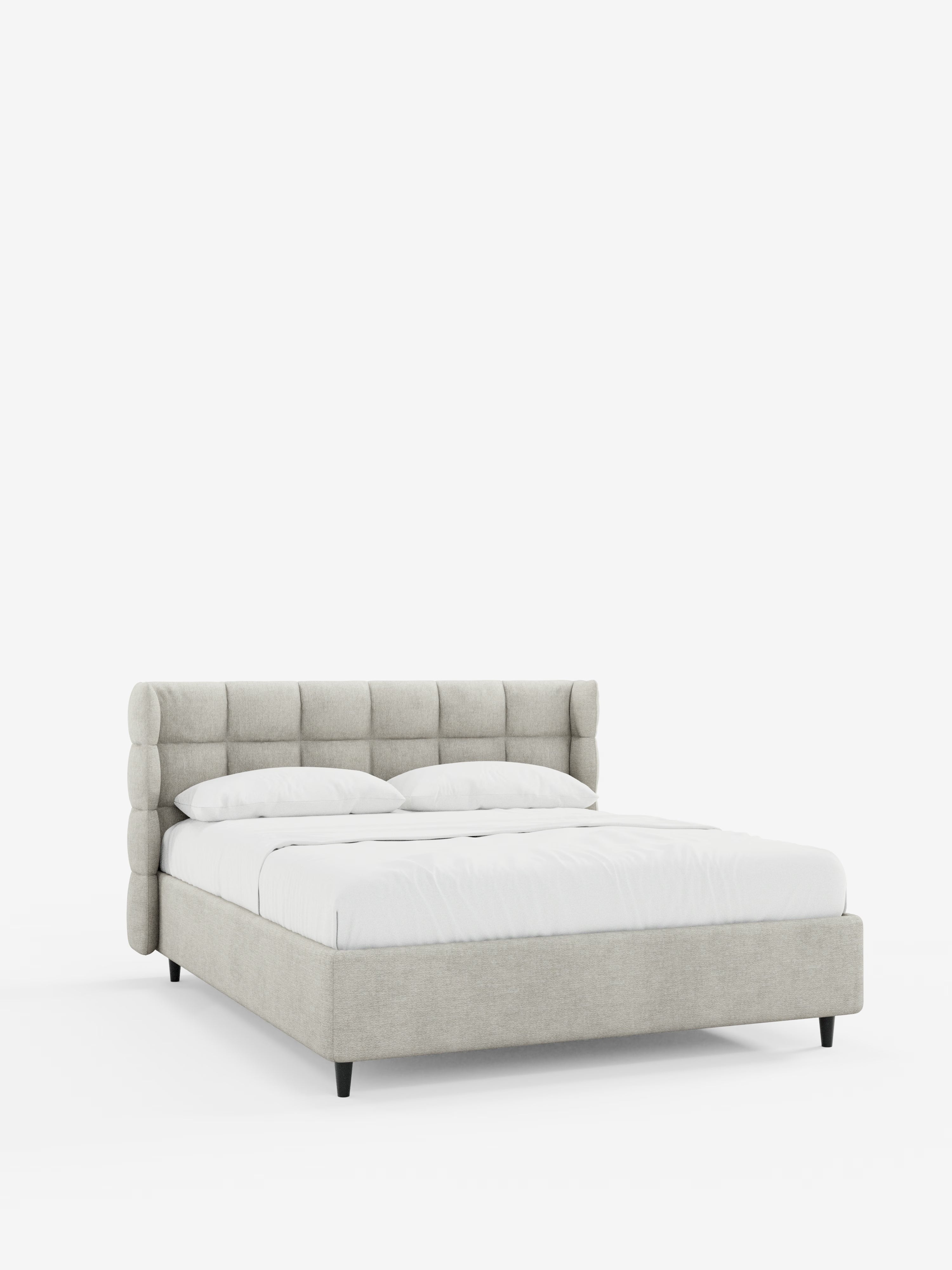 Il letto imbottito contemporaneo RAGNAR con contenitore e testiera capitonné avvolgente di Letti.store presenta un’elegante testiera in tessuto grigio chiaro certificato Oeko-Tex® con trapuntatura cilindrica e una struttura dal profilo basso. Il letto è rifatto con cura con lenzuola e cuscini bianchi, poggia su quattro corte gambe nere ed è posto su uno sfondo bianco a tinta unita.