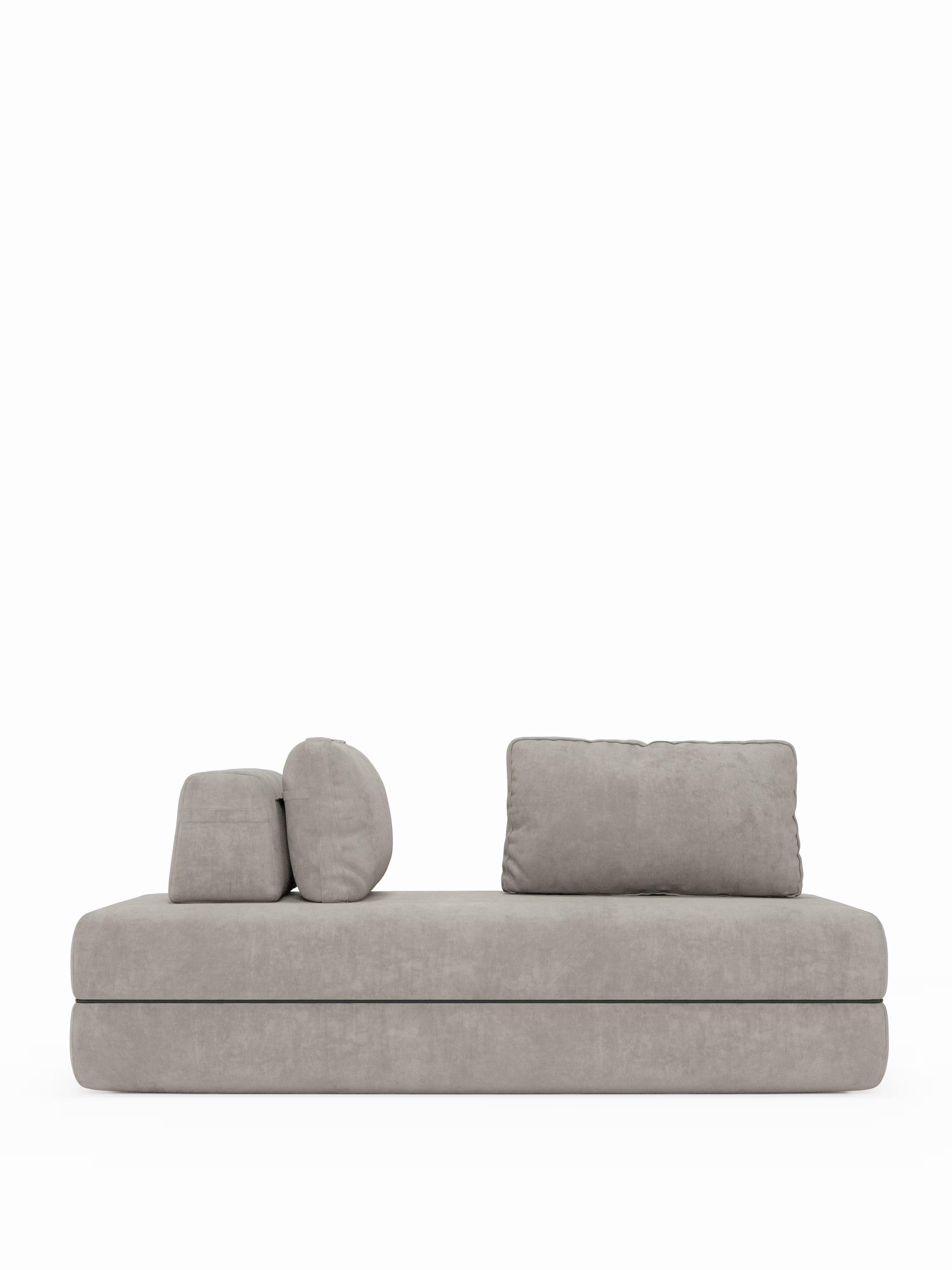 Un moderno divano letto matrimoniale Rift di Divani.Store in grigio chiaro, caratterizzato da una seduta rettangolare dal profilo ribassato e da tre cuscini dello schienale rimovibili — due rettangolari e uno rotondo — disposti sul lato sinistro, su uno sfondo bianco a tinta unita. Questo divano letto a 2 e 3 posti vanta schienali mobili ed è dotato di un materasso in memory foam di alta qualità, alto 22 cm, nella versione T31, per un comfort eccezionale.