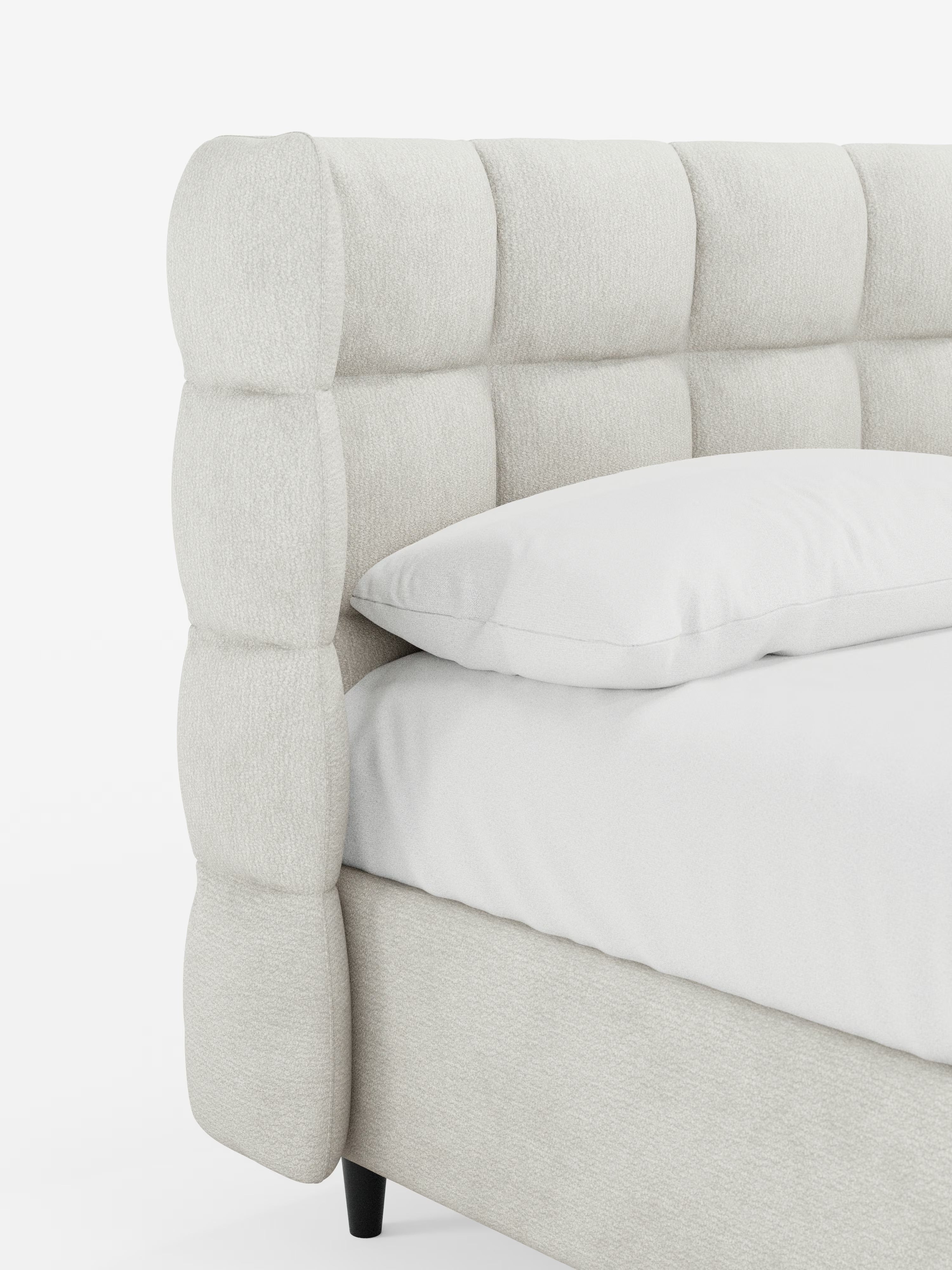 Un primo piano del letto imbottito RAGNAR con contenitore e testiera capitonné avvolgente di Letti.store, rivestito con un elegante tessuto certificato Oeko-Tex®. La testiera presenta ampie sezioni quadrate trapuntate in tessuto bianco, completate da un cuscino bianco e da un lenzuolo con angoli sul materasso. Lo sfondo è bianco e a tinta unita.