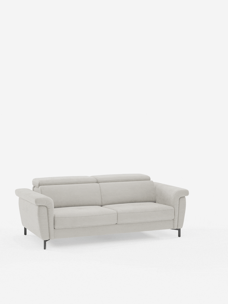 Un divano a due posti moderno, di colore grigio chiaro, con morbidi cuscini, braccioli arrotondati e sottili gambe nere, è posto al centro di uno sfondo bianco a tinta unita. Il divano letto di design Capri con piedini alti di Divani.Store è dotato di poggiatesta regolabili ed è rivestito in raffinato tessuto effetto velluto T30 antimacchia, che unisce comfort e artigianato italiano contemporaneo.