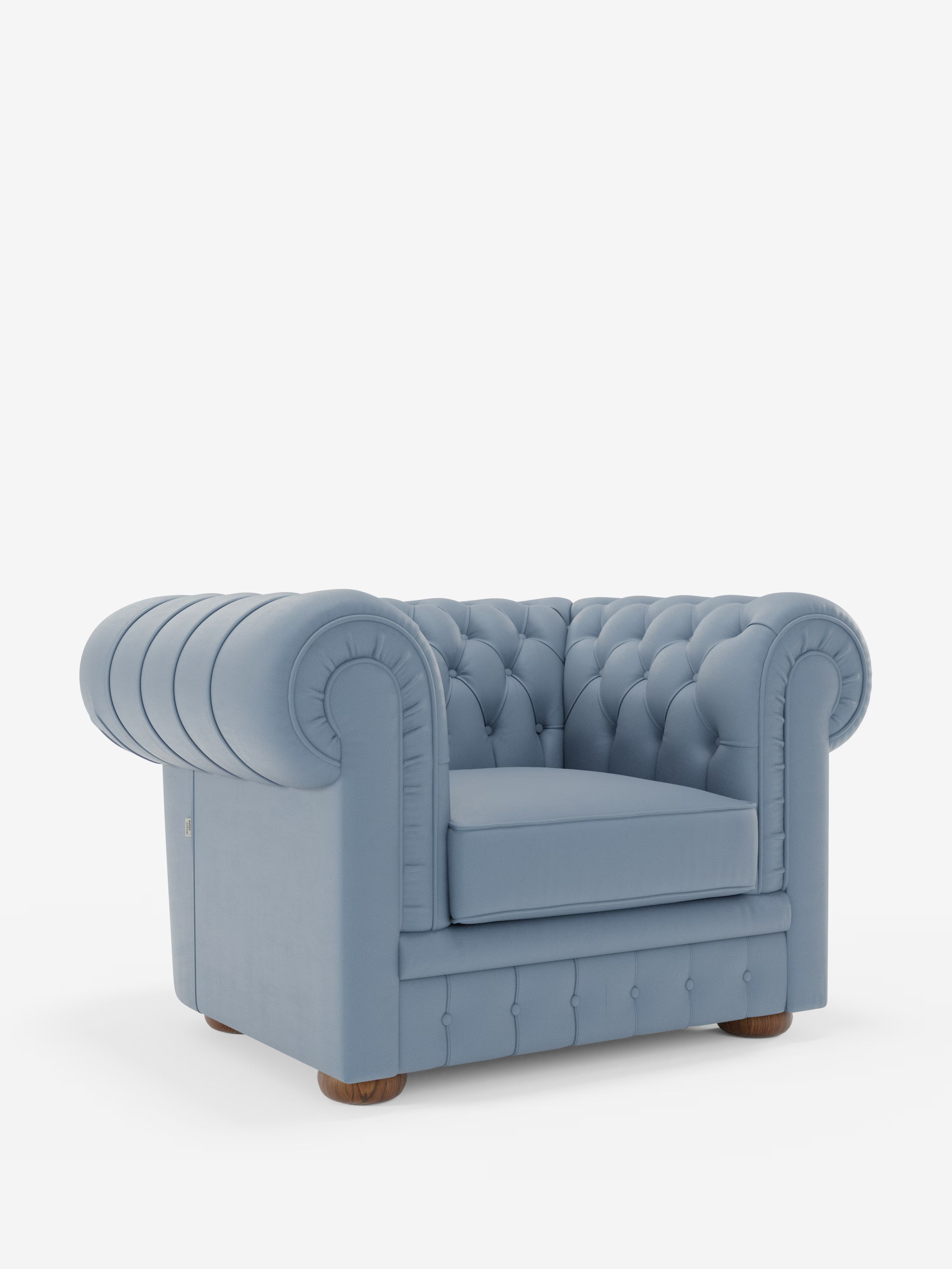 Una poltrona Chester azzurra in vera pelle spessorata con capitonné artigianale di Divani.Store, caratterizzata da un rivestimento trapuntato con bottoni decorativi, braccioli e schienale arrotondati e piedini in legno, è posizionata su uno sfondo bianco a tinta unita.