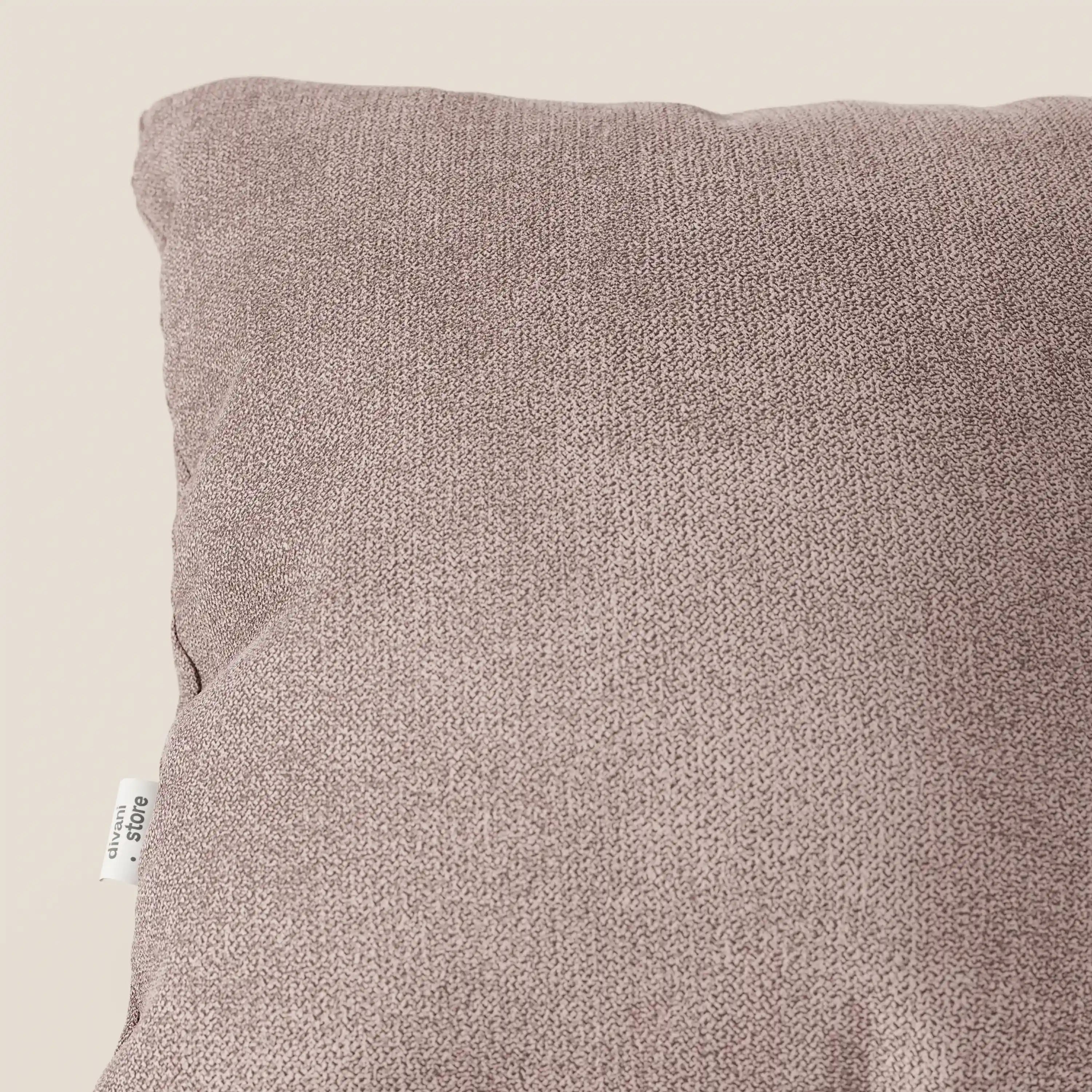 Primo piano del cuscino Destiny 45x45 cm in T02 rosa di Divani.Store, realizzato in morbido tessuto impermeabile. Una parte dell'elegante cuscino con una piccola etichetta di cucitura bianca è visibile su uno sfondo neutro.