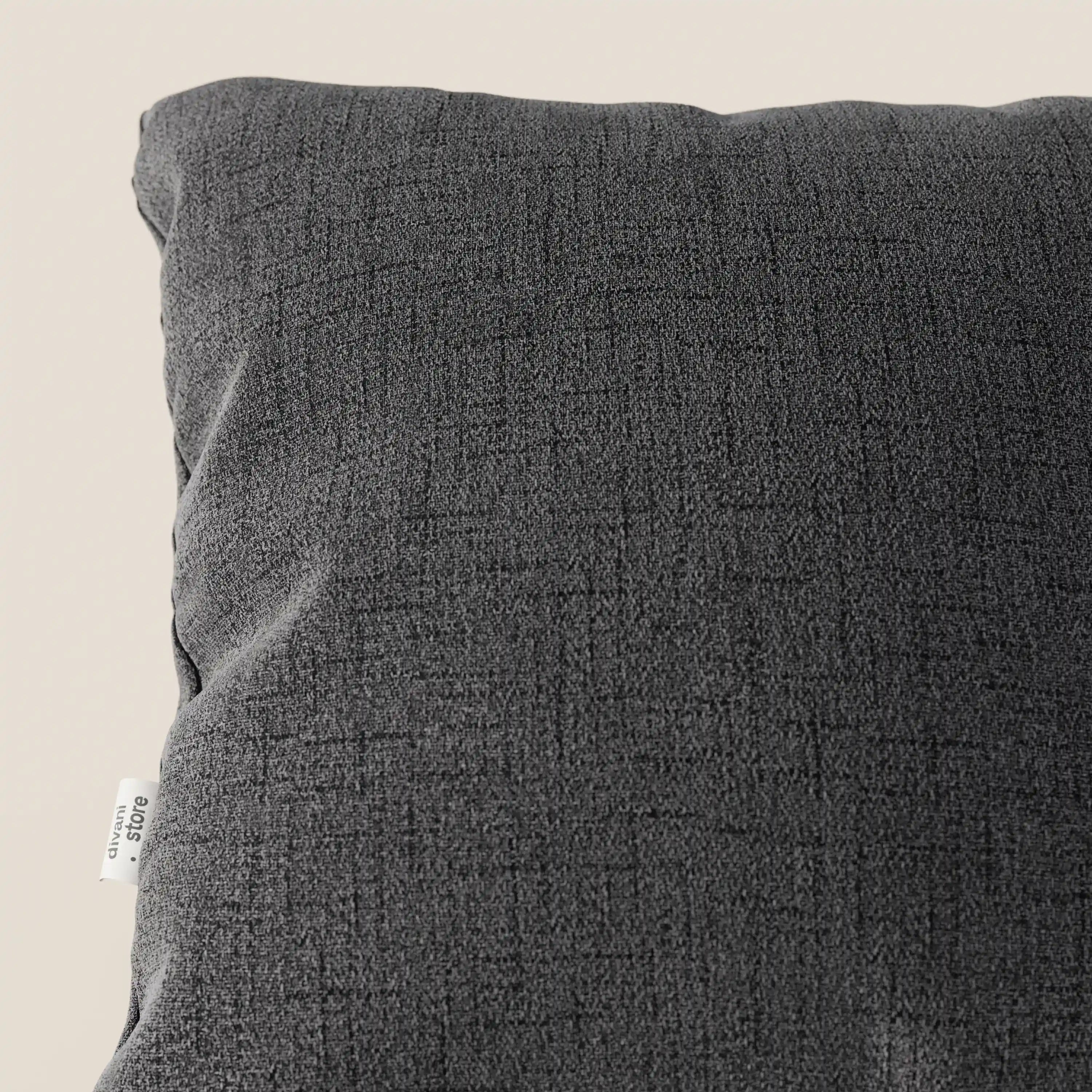 Primo piano dell'angolo superiore sinistro del cuscino Felis in tessuto morbido impermeabile T03 antracite di Divani.Store, che mostra un sottile motivo incrociato e una targhetta bianca sulla sinistra. Lo sfondo è un semplice beige chiaro.