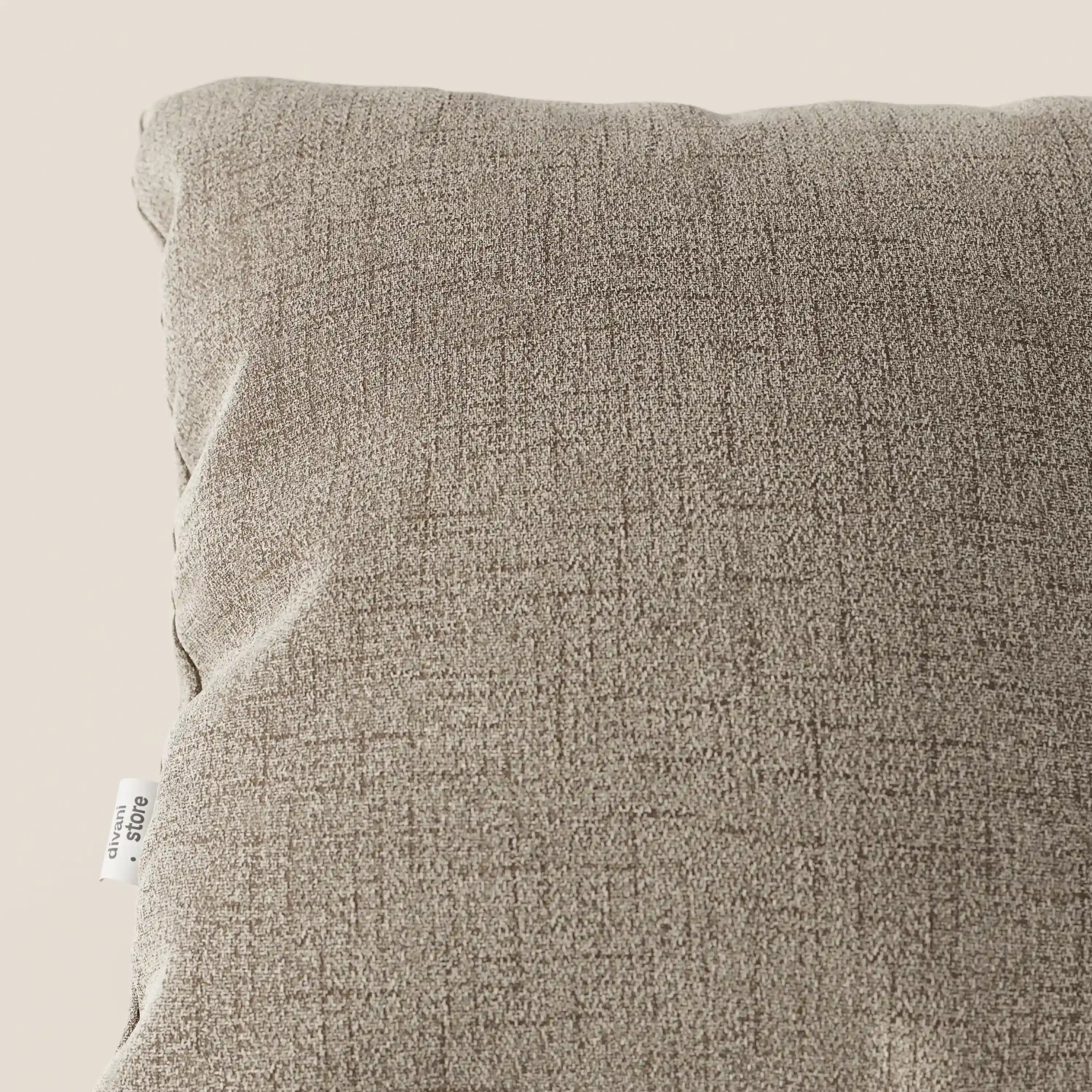 Un primo piano del cuscino Felis di Divani.Store in T03 beige mostra il suo tessuto morbido e impermeabile con una sottile trama incrociata e una piccola etichetta bianca cucita nella cucitura, su uno sfondo beige chiaro.