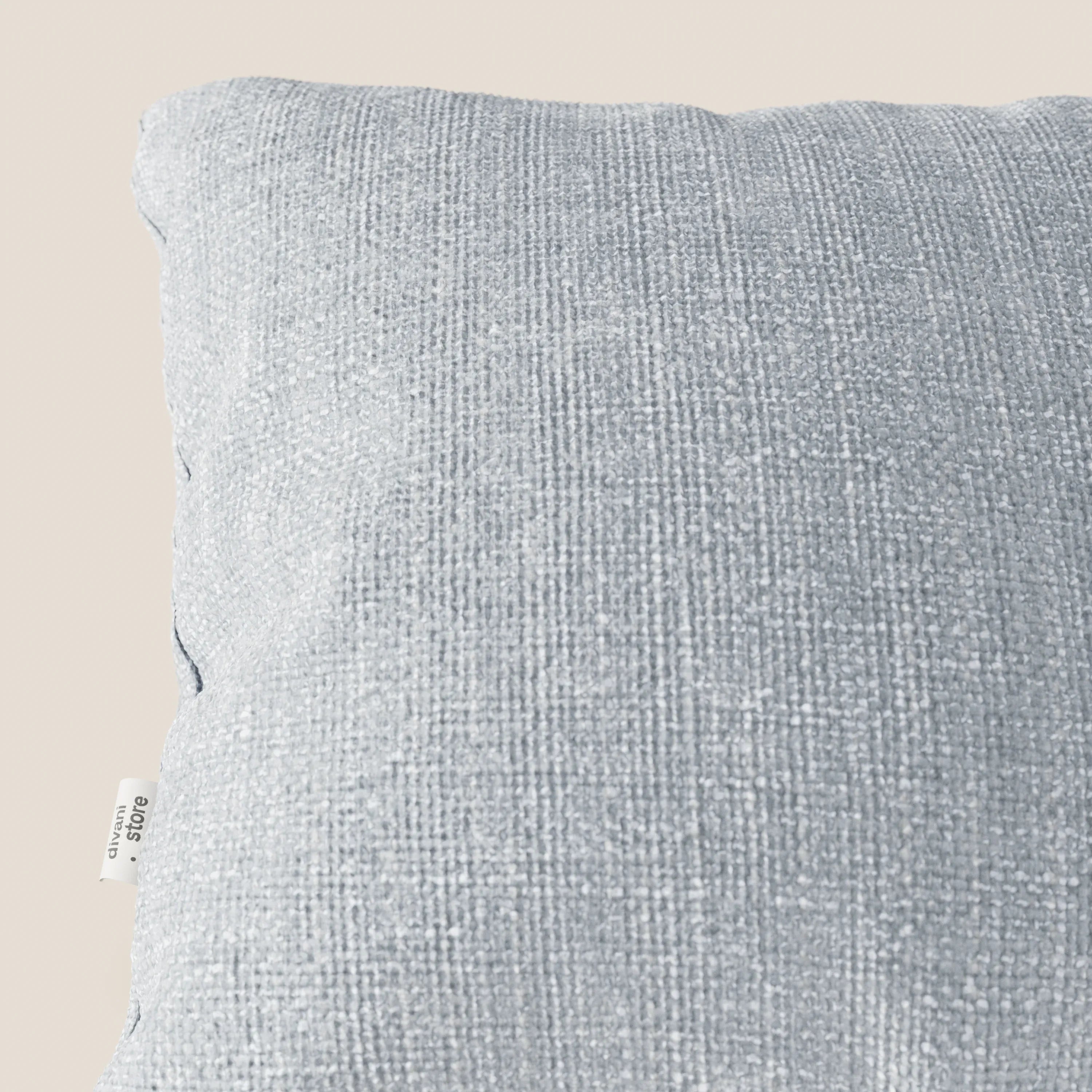 Primo piano del cuscino Lyon 45x45 cm di Divani.Store in morbido tessuto intrecciato impermeabile T06 ghiaccio, su sfondo beige. Una piccola etichetta di tessuto bianco è visibile sulla cucitura sinistra e ne evidenzia la qualità e la consistenza.