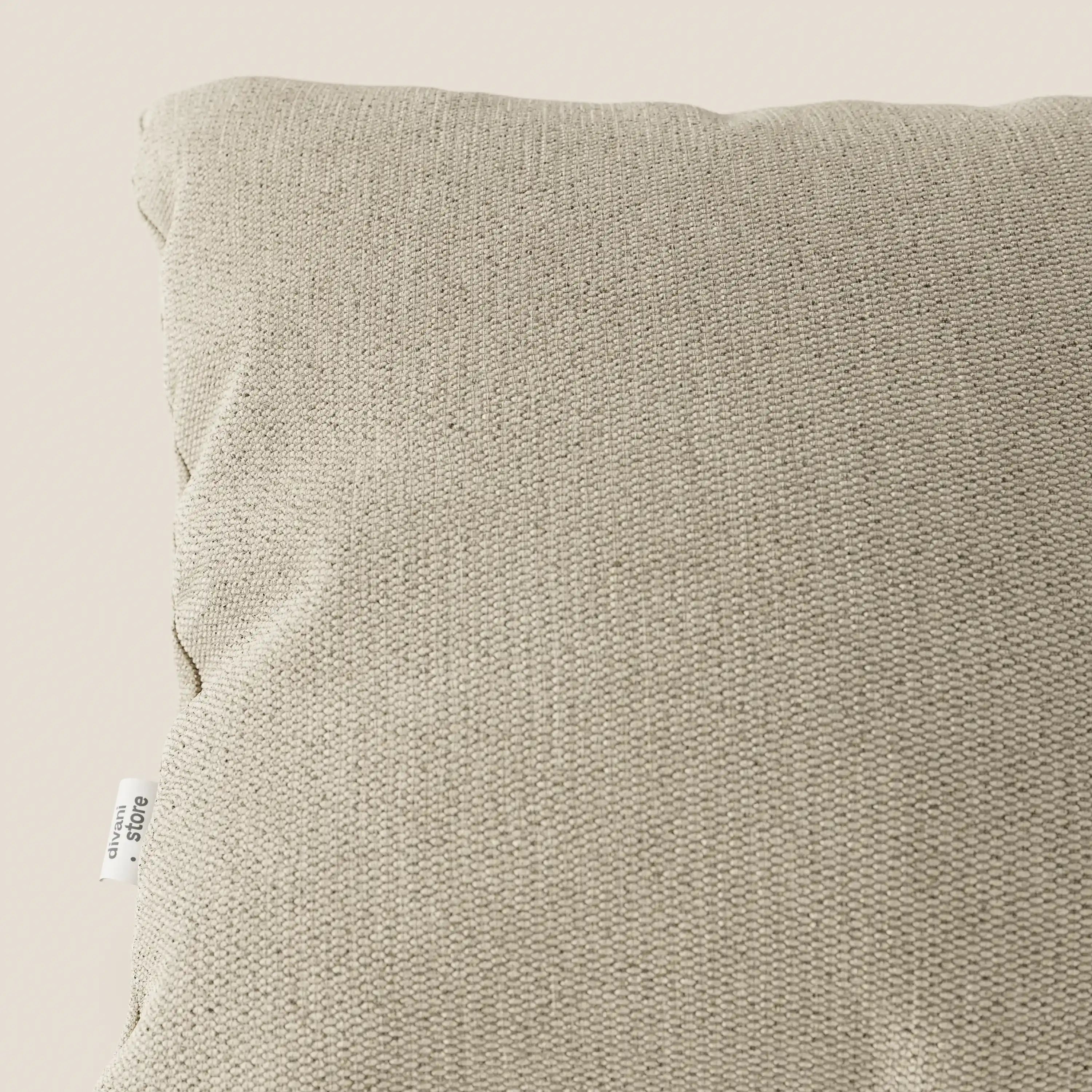 Primo piano dell'angolo superiore sinistro del cuscino Miami 45x45 T14 beige di Divani.Store, realizzato in tessuto morbido impermeabile, con una piccola etichetta bianca e una trama a maglia visibile su uno sfondo chiaro.