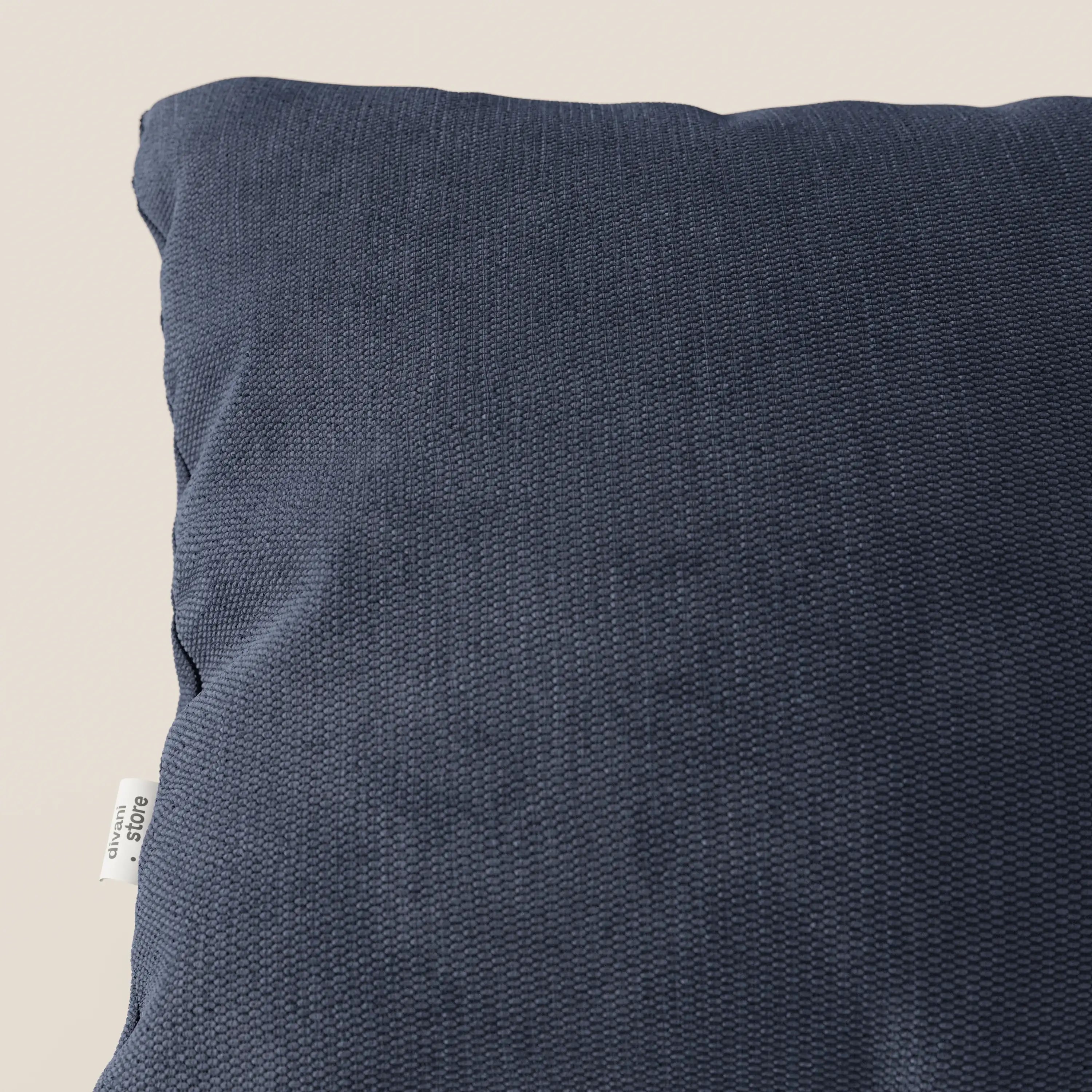 Primo piano del cuscino Miami di Divani.Store in tessuto impermeabile T14 blu, caratterizzato da un design strutturato, un coperchio lavabile e una piccola etichetta bianca sulla sinistra: perfetto per arredare la casa con stile e praticità.